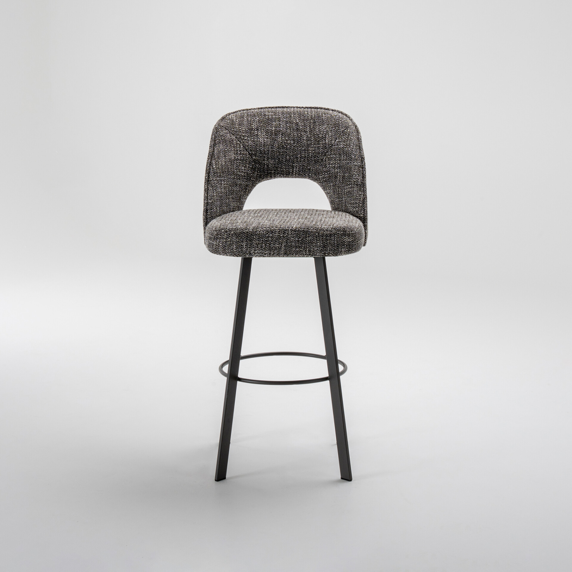 A modern bar stool with a textured gray fabric seat and backrest, featuring a cutout in the back, on slender black metal legs with a circular footrest, against a white background.