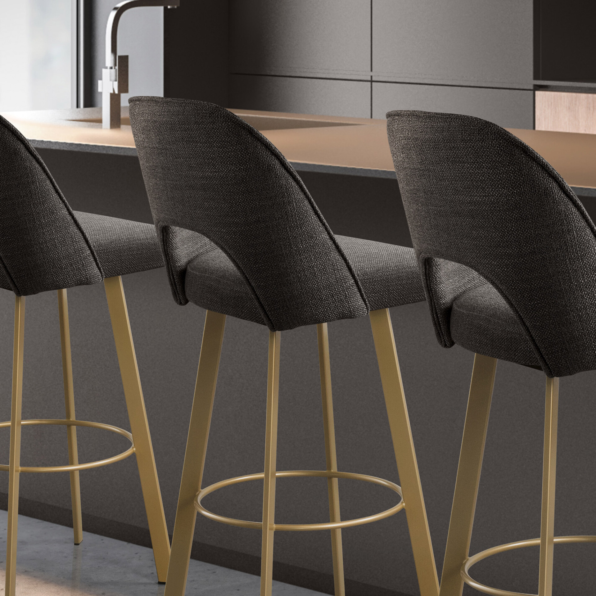 Three modern dark gray fabric bar stools with golden metal legs and footrests, positioned at a sleek kitchen island with a light brown countertop and dark gray cabinetry.