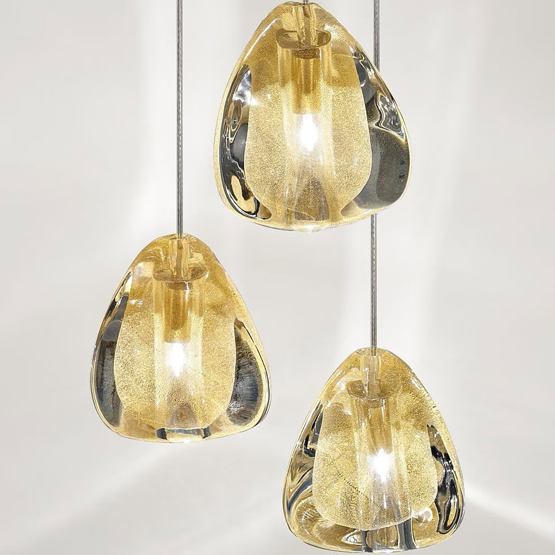 Three golden, teardrop-shaped glass pendant lights hang from thin wires against a white background, emitting a warm, sparkling glow.