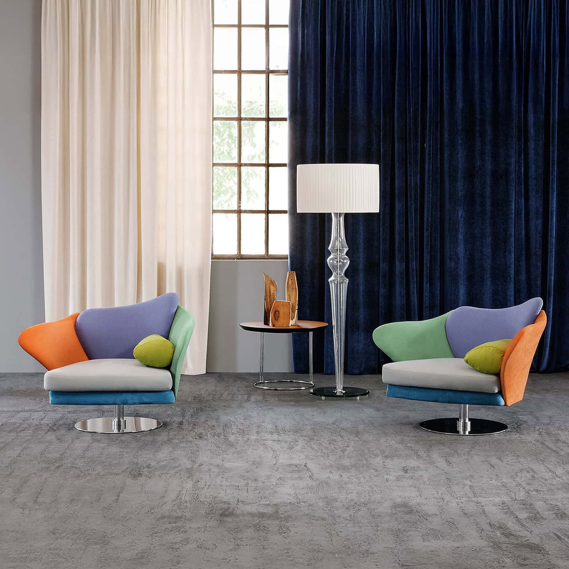 Colorful pair of Flower Armchairs in orange, blue, green, and purple fabric set in a modern living room with blue drapery backdrop