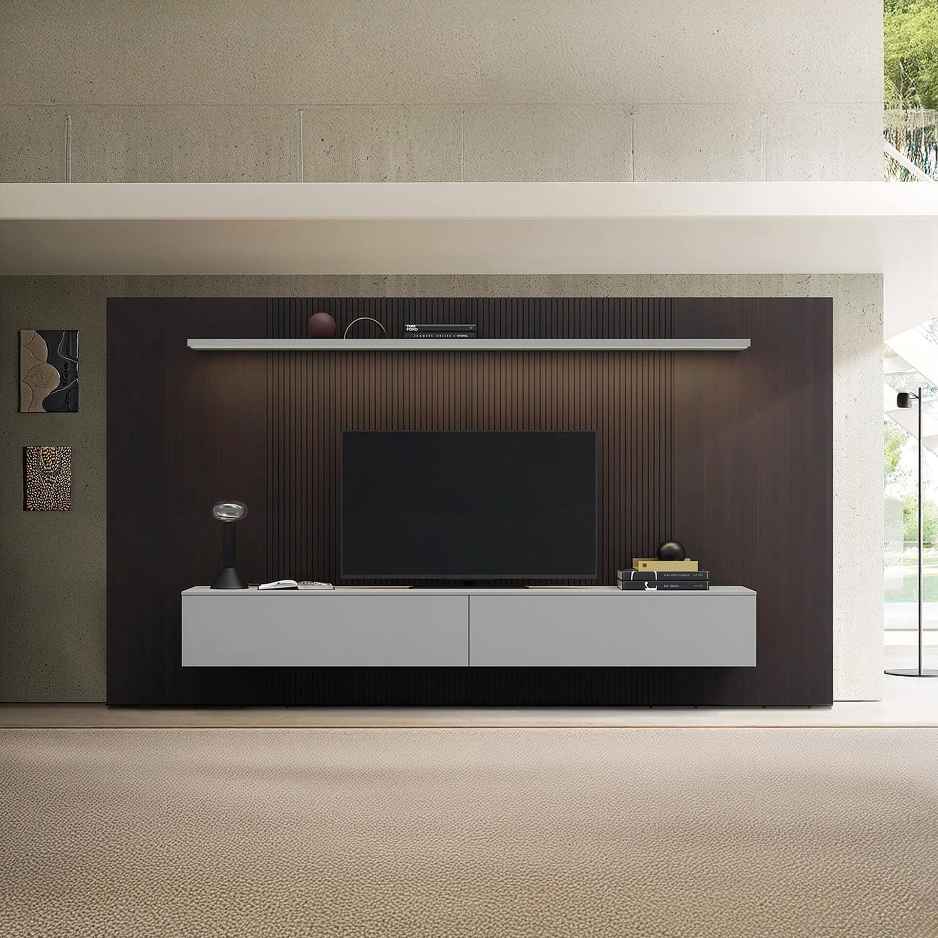 A modern living room with a dark wood media wall, a large TV, a light gray floating console, and a lighted shelf. Two abstract art pieces hang on the concrete wall to the left. The floor is covered in a light beige carpet.