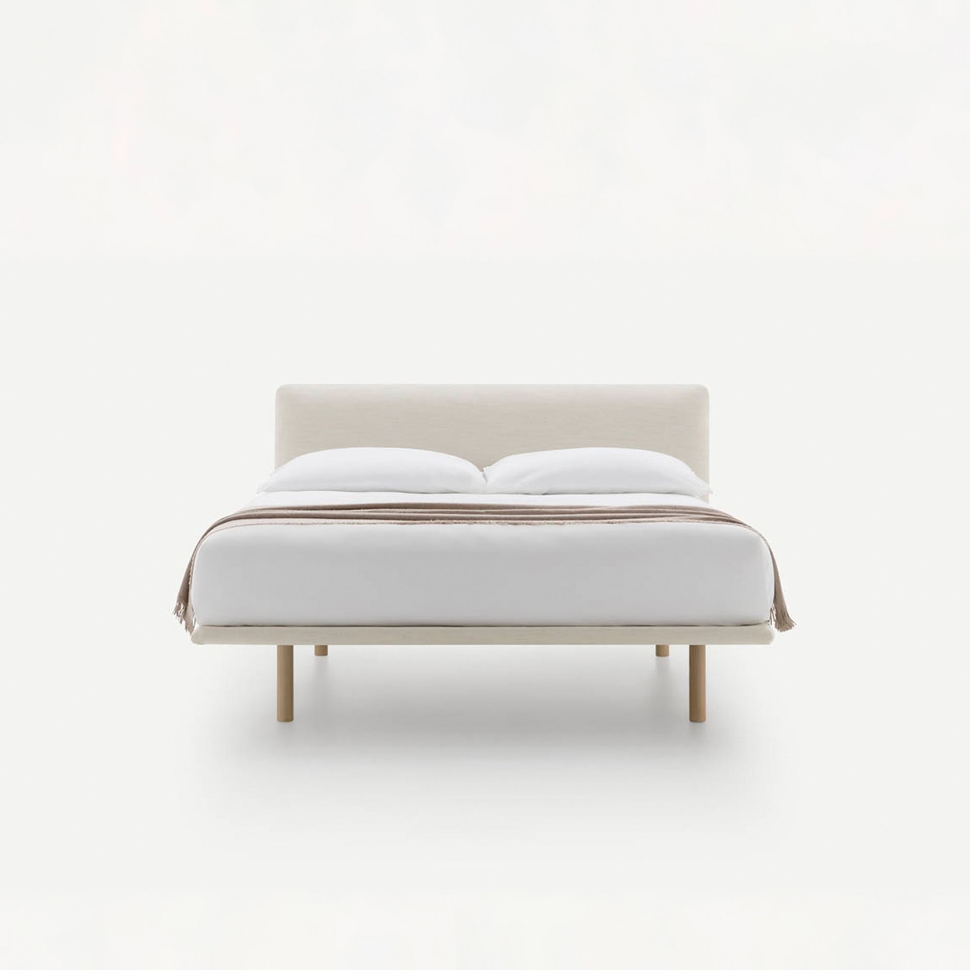 A modern, minimalist bed with a light beige upholstered frame, white bedding, and a brown throw blanket, on a white background.