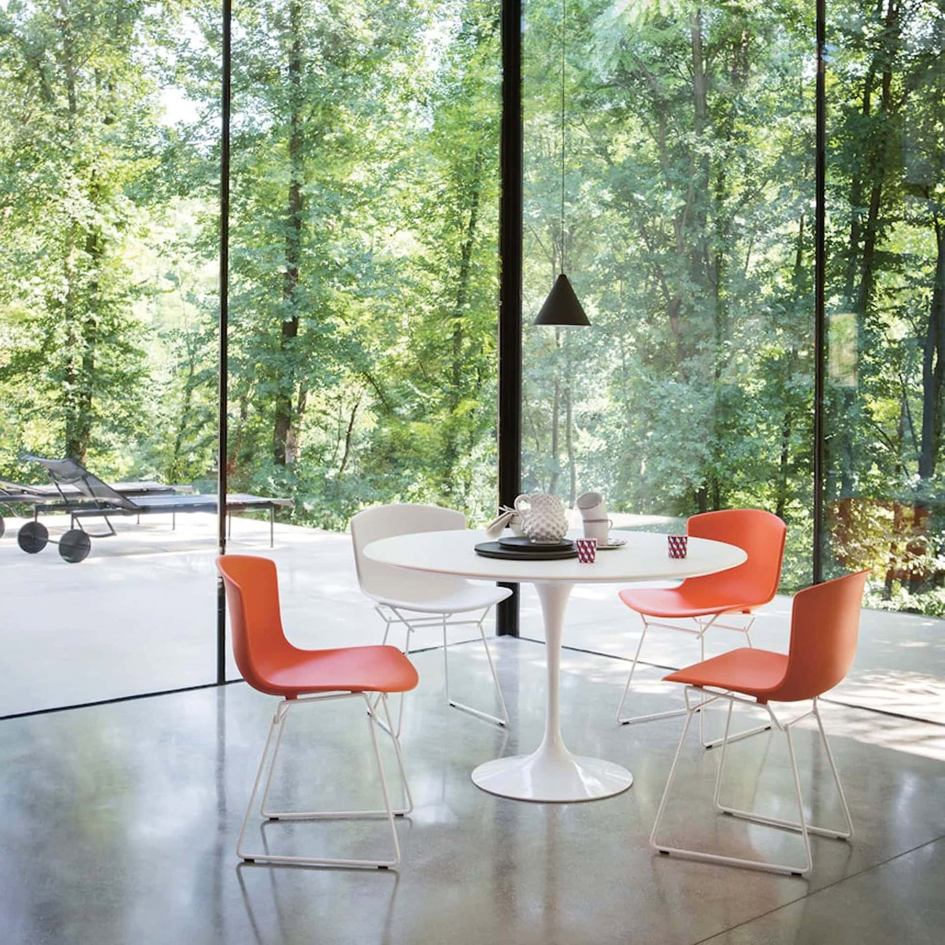 White Saarinen Dining Table with orange chairs in a bright glass-walled room.