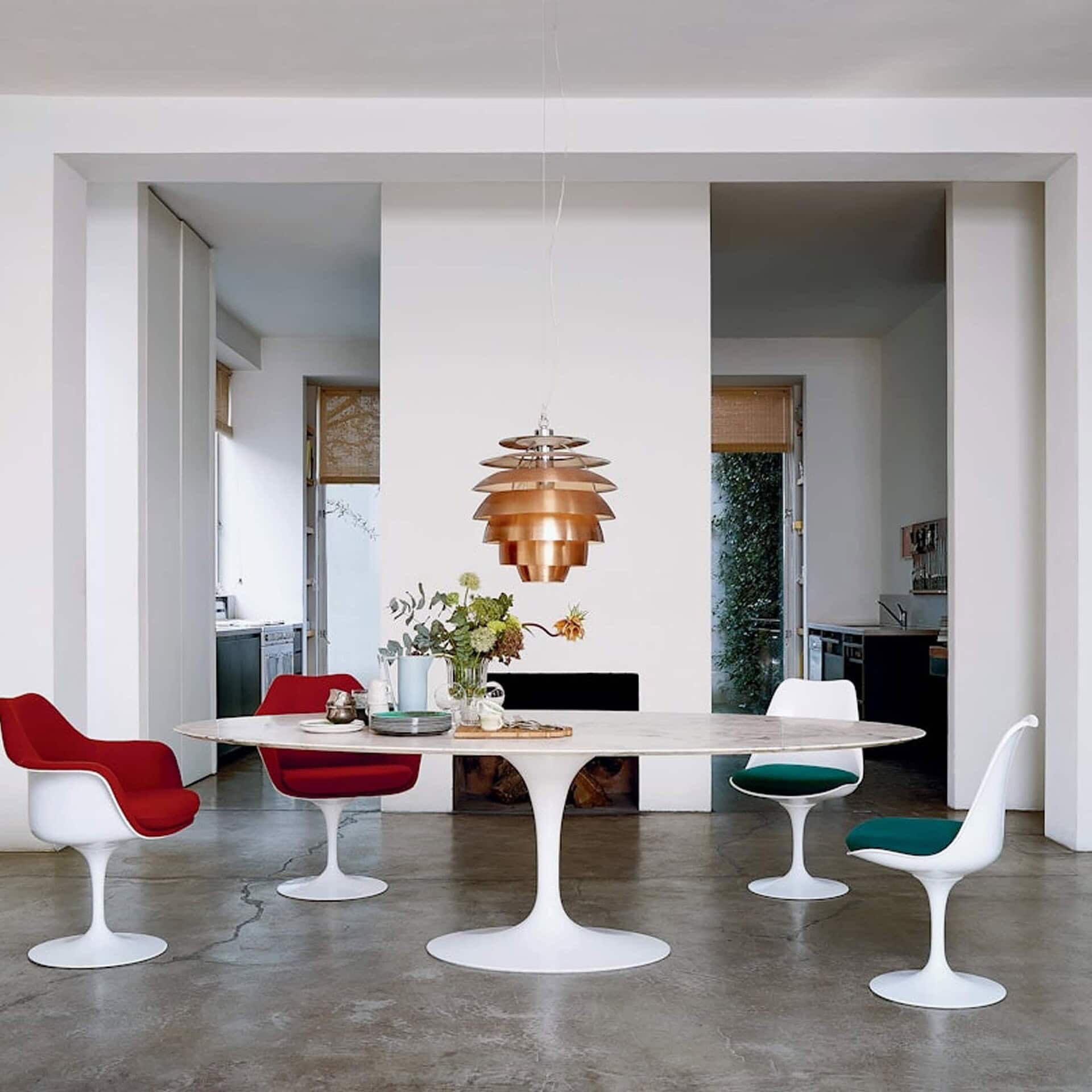 Saarinen Dining Table with round white top in a retro-inspired interior with red chairs.