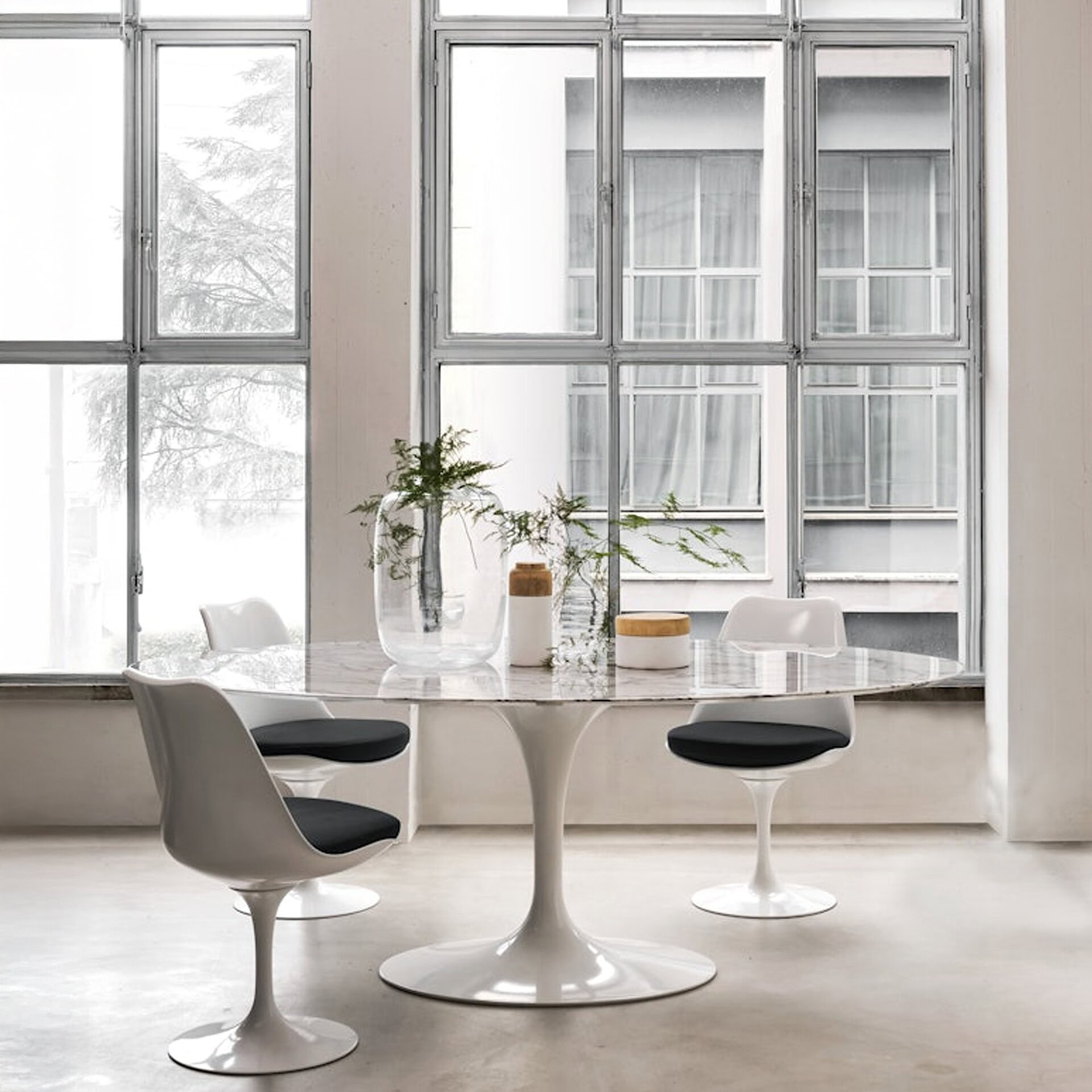 Round Saarinen Dining Table in white with black chairs in a minimalist white interior.