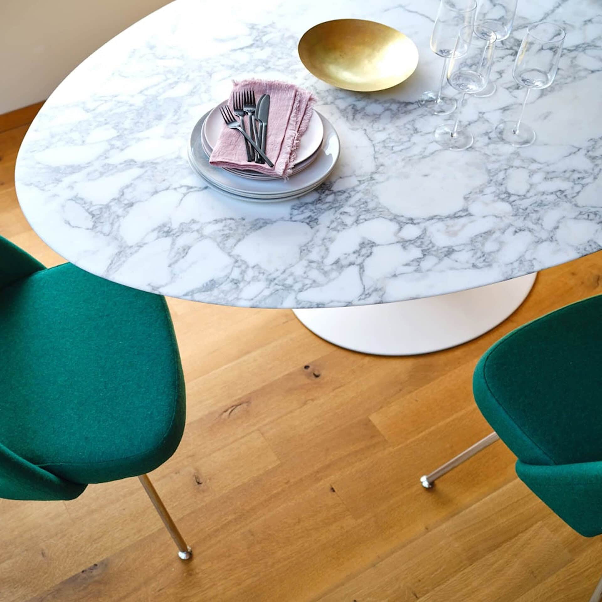 Close-up of Saarinen Dining Table with white marble top, styled with green dining chairs.
