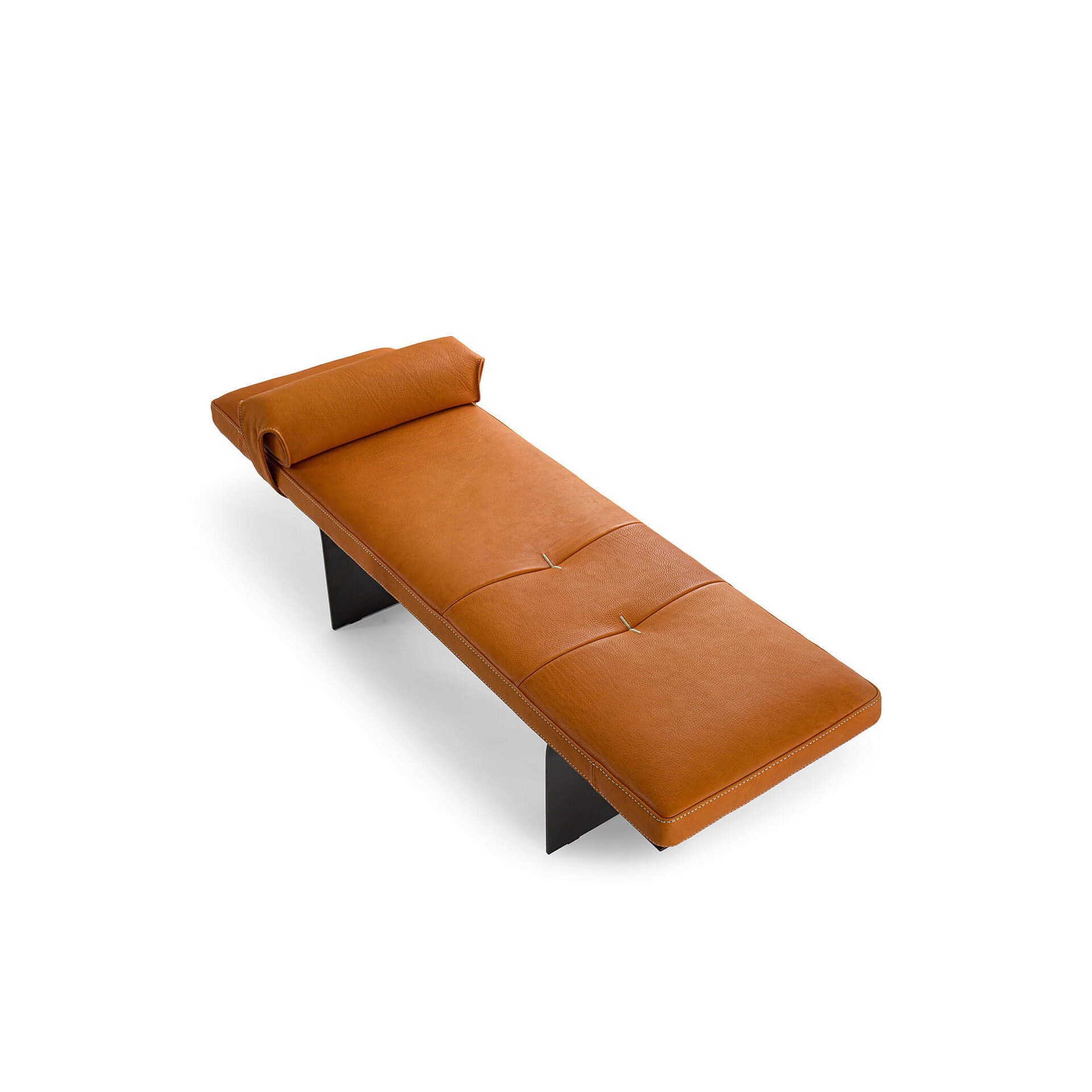 A modern tan leather chaise lounge with a rolled headrest, subtle tufting, and dark angular metal legs, set against a white background.