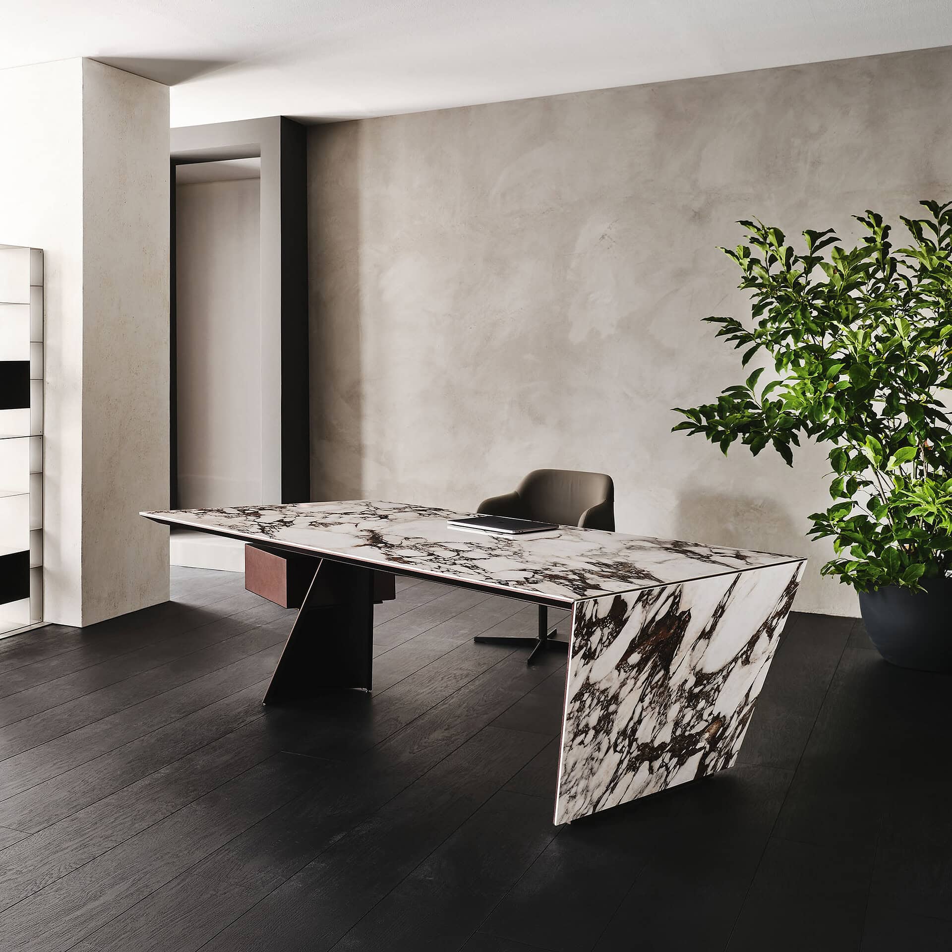 Modern marble office desk with black chair and large potted plant in minimalist workspace.