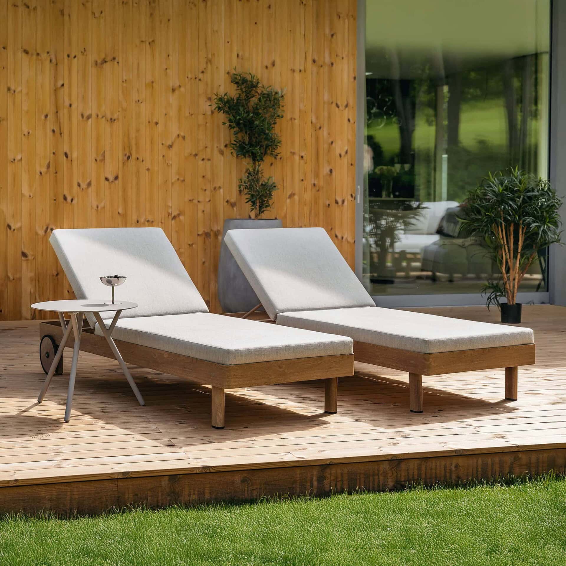 Modern outdoor lounge chairs on a wooden deck with potted plants and a glass wall.