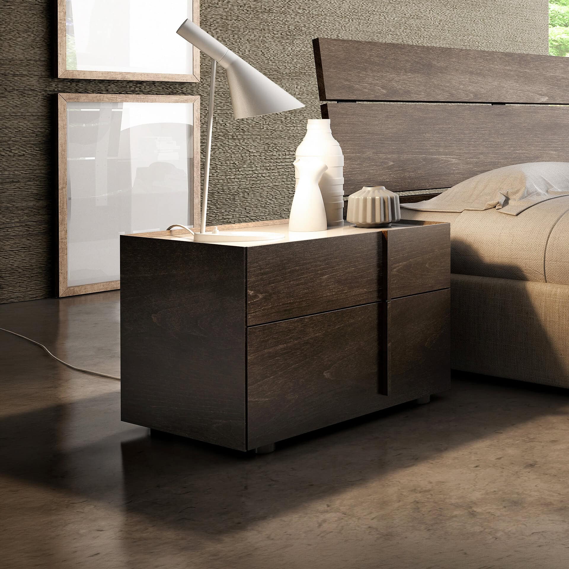 A modern bedroom with a dark wood nightstand, a grey lamp, and ceramic vases next to a beige bed. Light wooden frames lean against a textured wall, and strong light casts shadows on the dark floor.