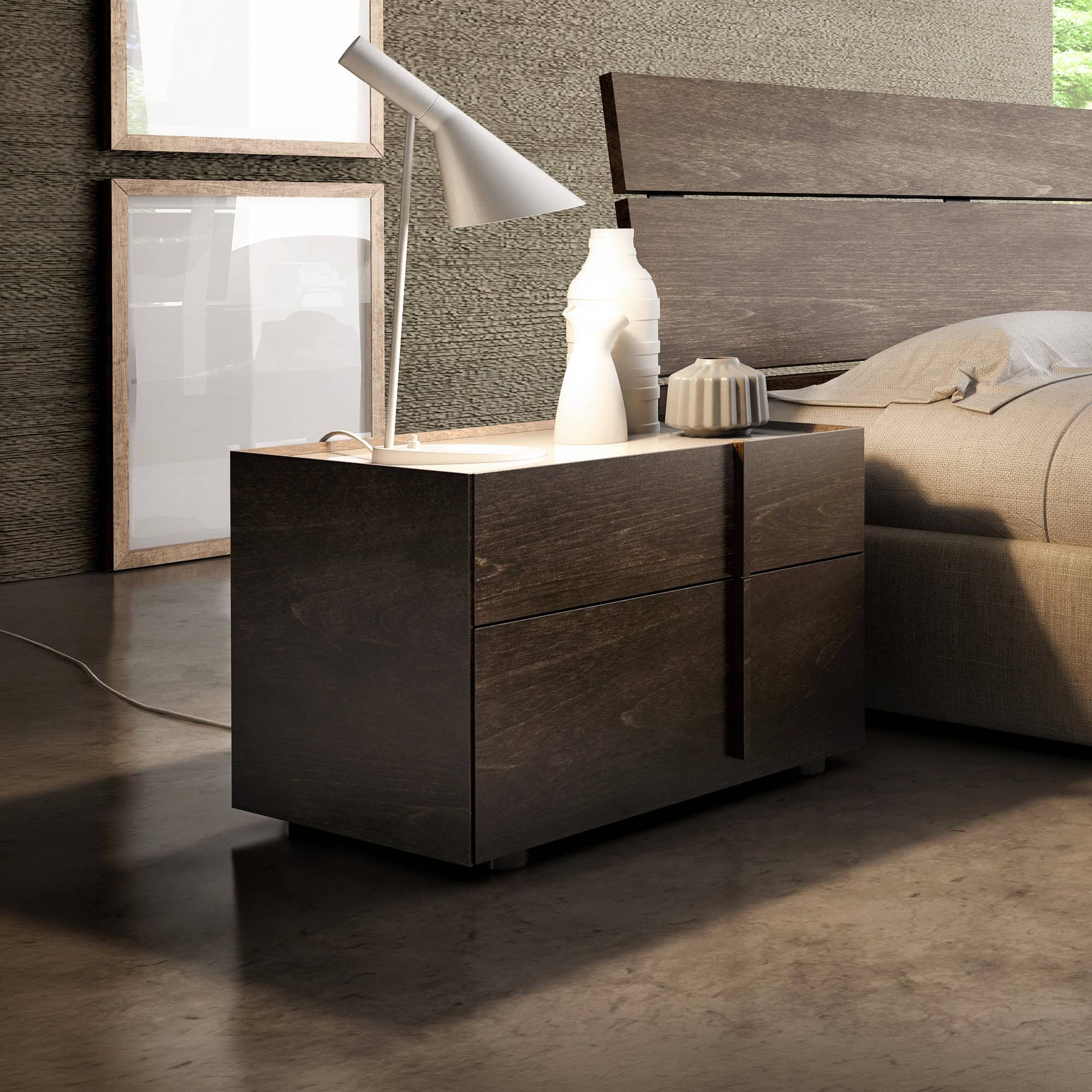 A modern bedroom with a dark wood nightstand, a grey lamp, and ceramic vases next to a beige bed. Light wooden frames lean against a textured wall, and strong light casts shadows on the dark floor.