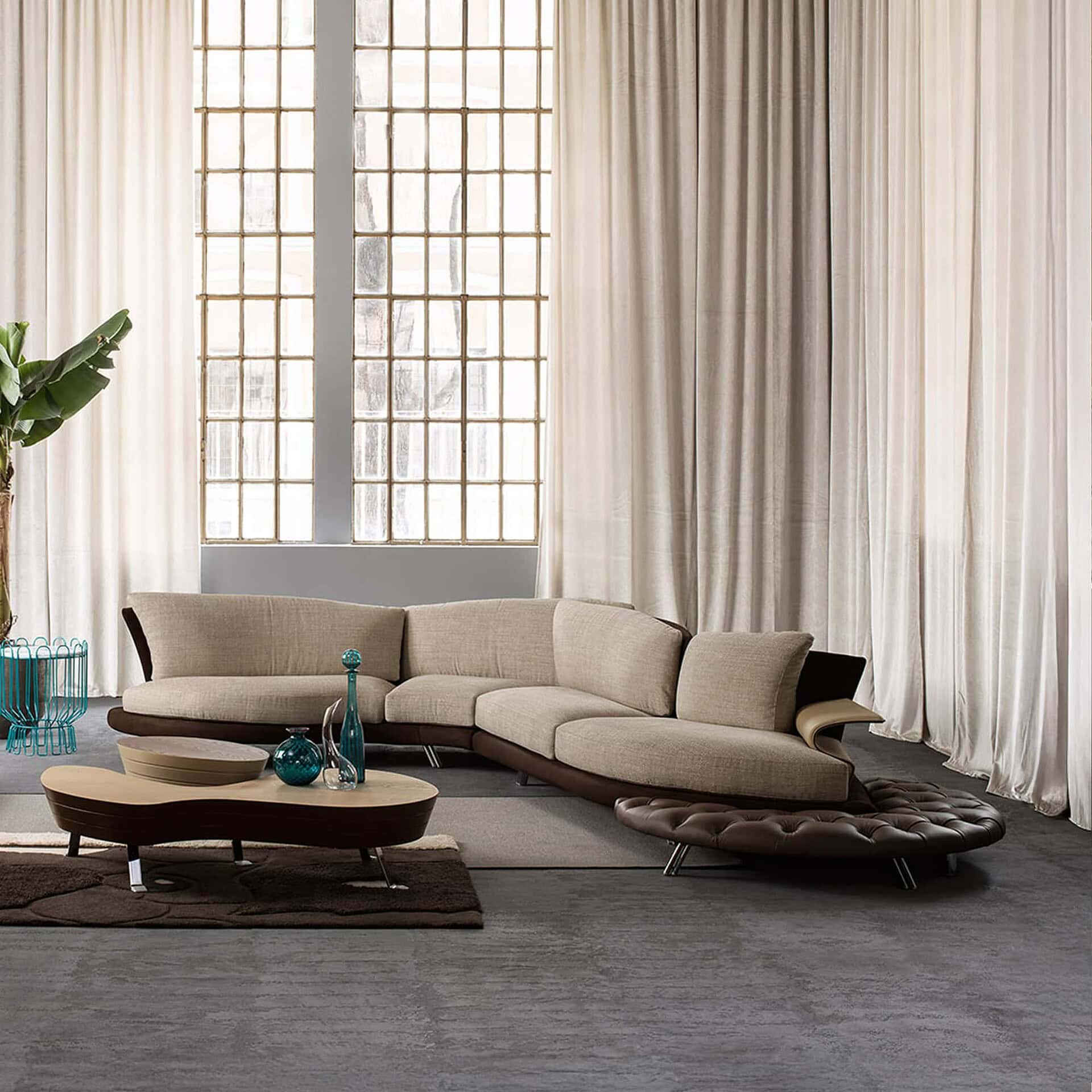 Close-up of a taupe Super Roy sofa corner module in front of a textured green wall and sculptural art.