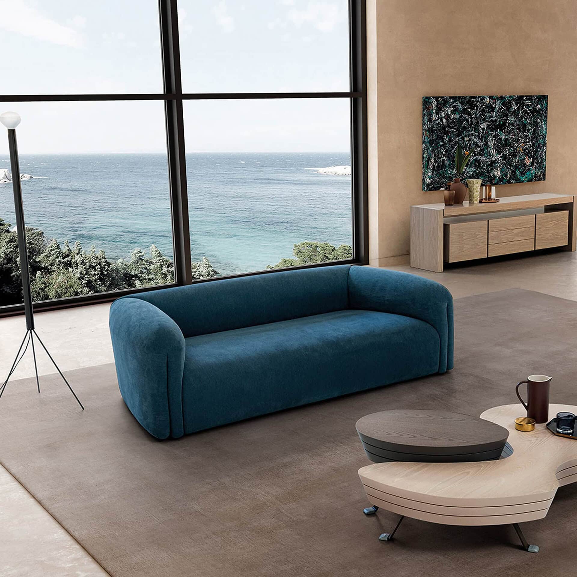 Quentin Linear Upholstered Sofa in teal fabric with curved arms, styled in a bright modern living space with large windows.