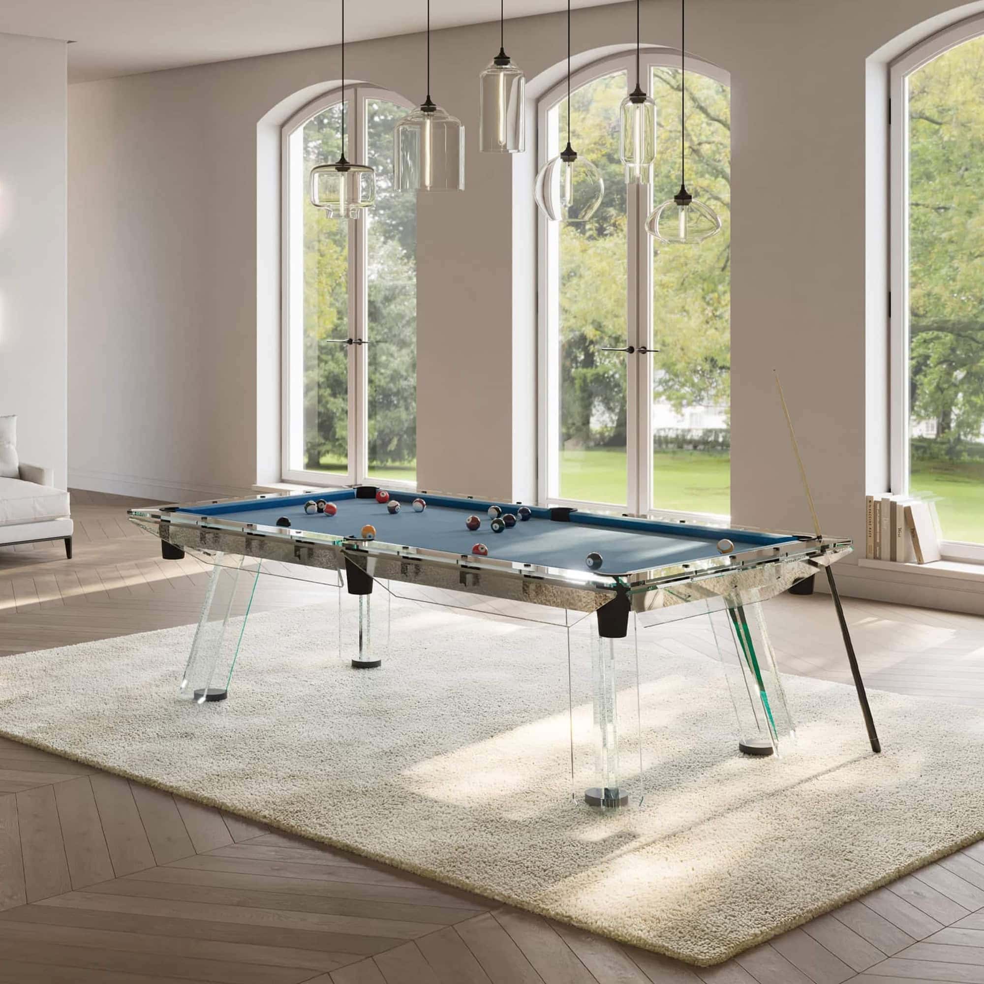 Modern glass pool table with sleek design and pendant lighting in stylish living space.