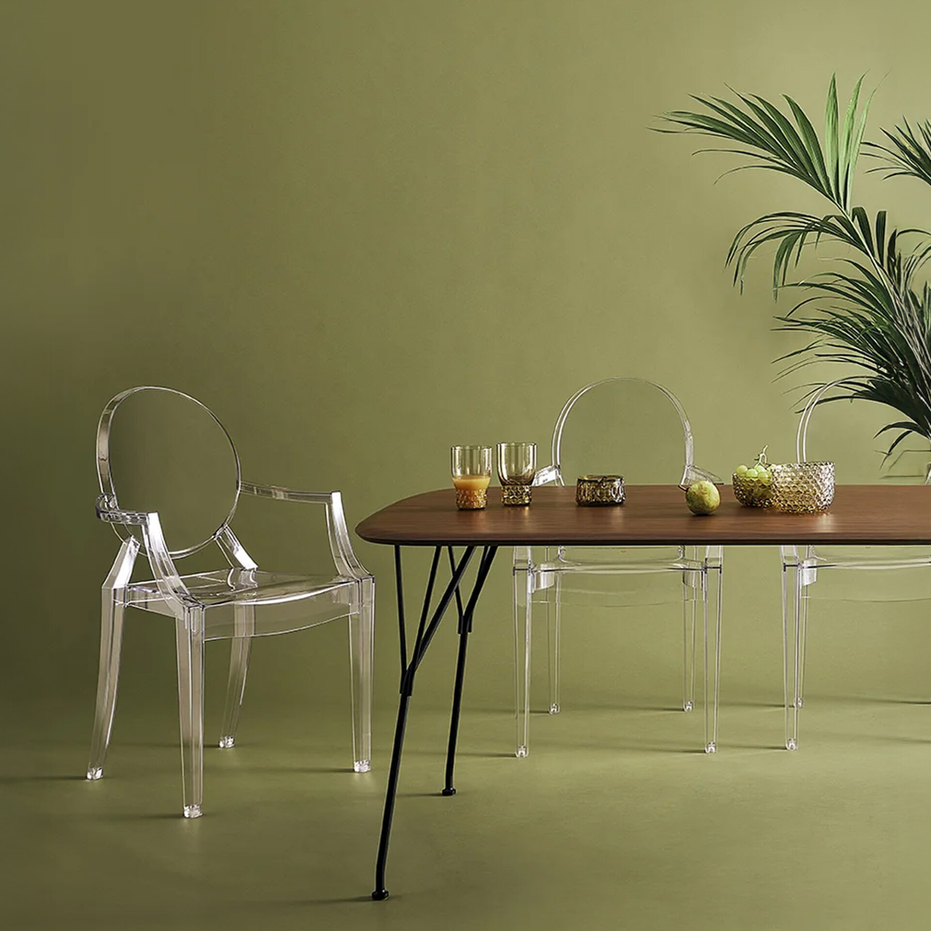 Louis Ghost Chairs around a minimalist dining table with a green backdrop