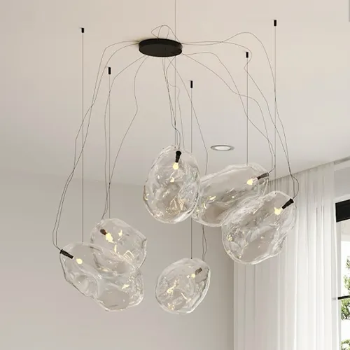 A modern chandelier with multiple irregular, clear glass pendants suspended by thin black wires from a central black ceiling mount, illuminating a white room.