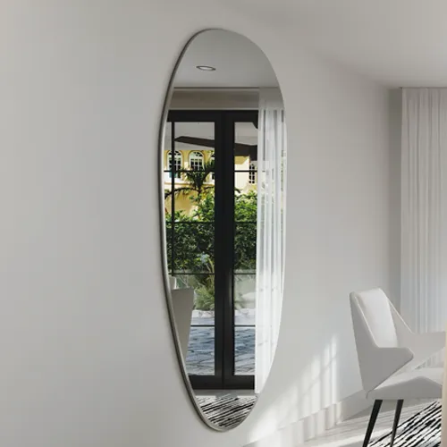 A large, vertical oval mirror on a white wall reflects a yellow building, green trees, and a glass door. A modern white armchair and patterned rug are visible to the right.