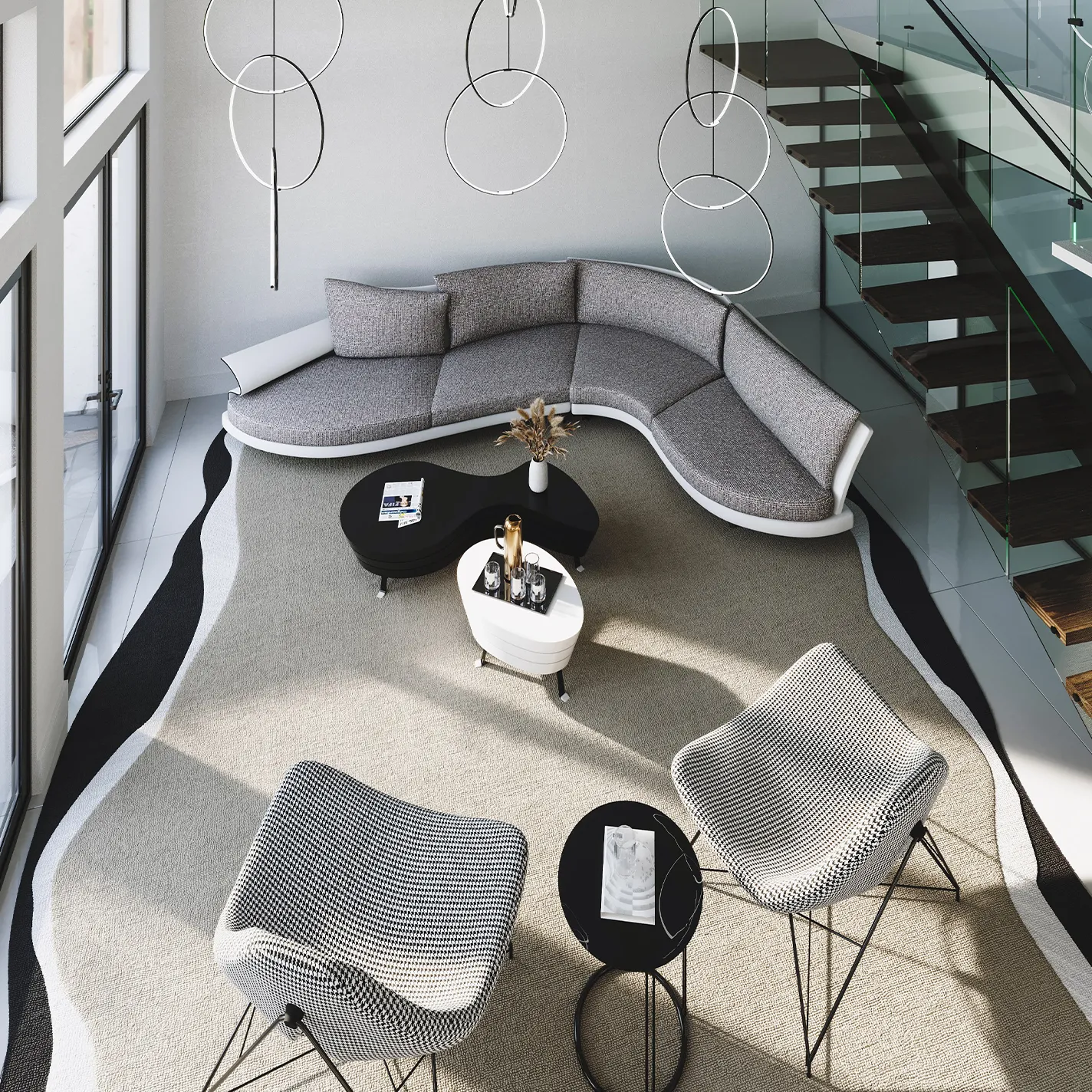 High-angle view of a modern living room with a curved gray sectional sofa, two black and white patterned armchairs, black coffee tables, and a glass staircase. Circular pendant lights hang from the high ceiling, and a large area rug with a wavy black and white border covers the floor.