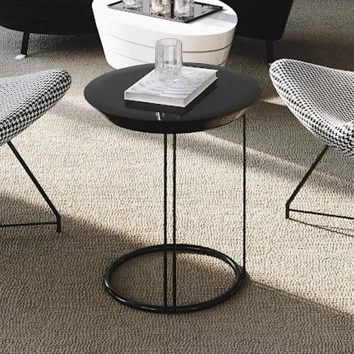 A black circular side table with a glass and white book, flanked by black and white patterned chairs on a light textured carpet.