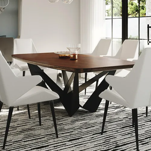A modern dining room featuring a dark wood table with a sculptural black metal base, surrounded by white upholstered chairs. A black and white striped rug covers the floor, and a large window with sheer curtains is visible in the background.