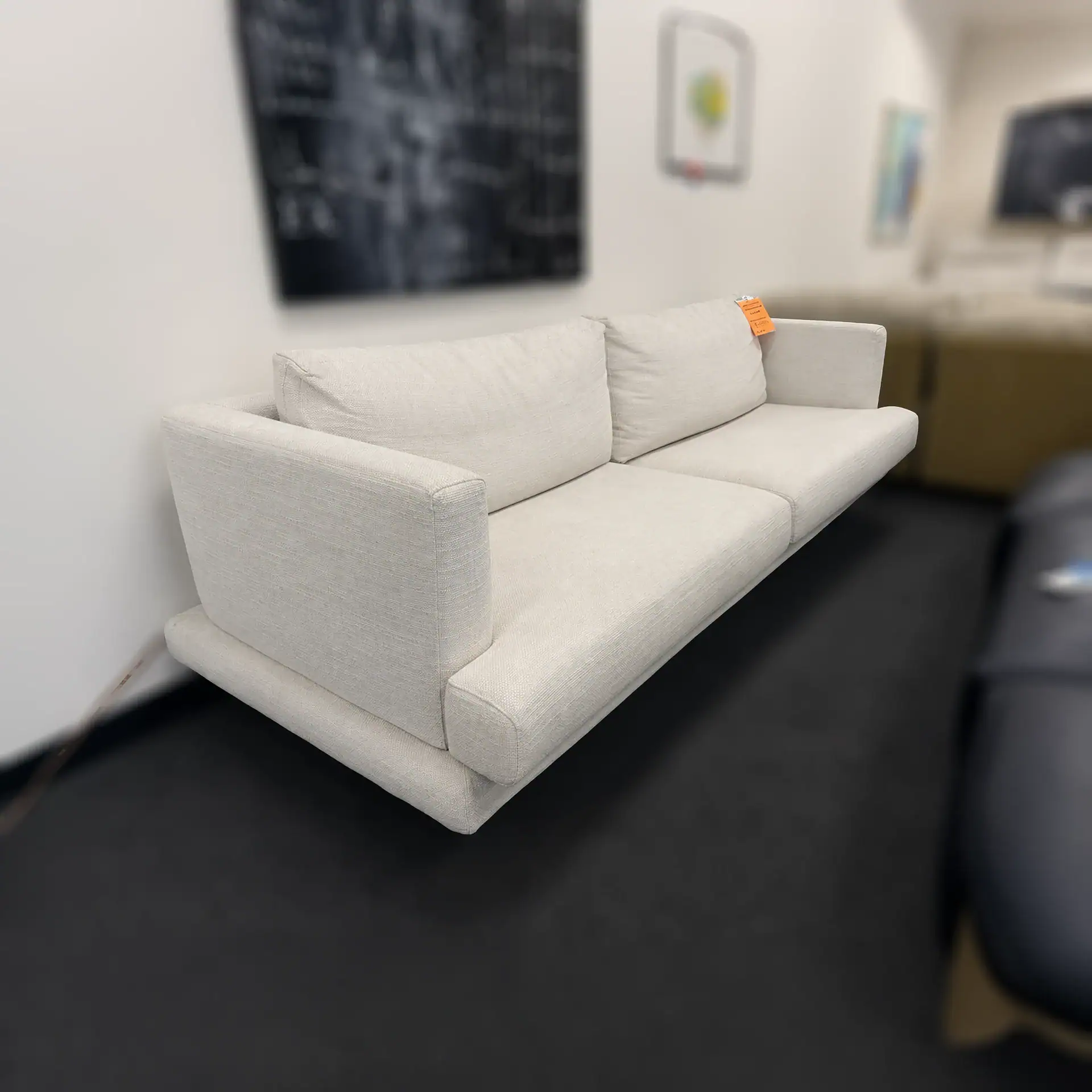 Modern white Mercury sofa in showroom with artwork on wall.