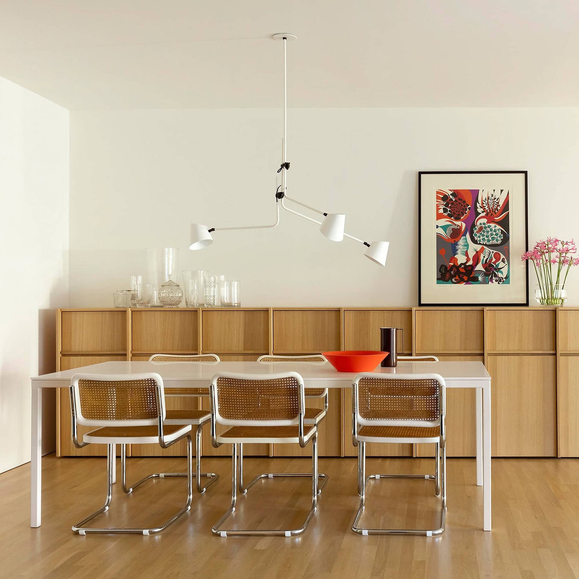 Modern dining room with wooden sideboard, white table, and contemporary adjustable chandelier.