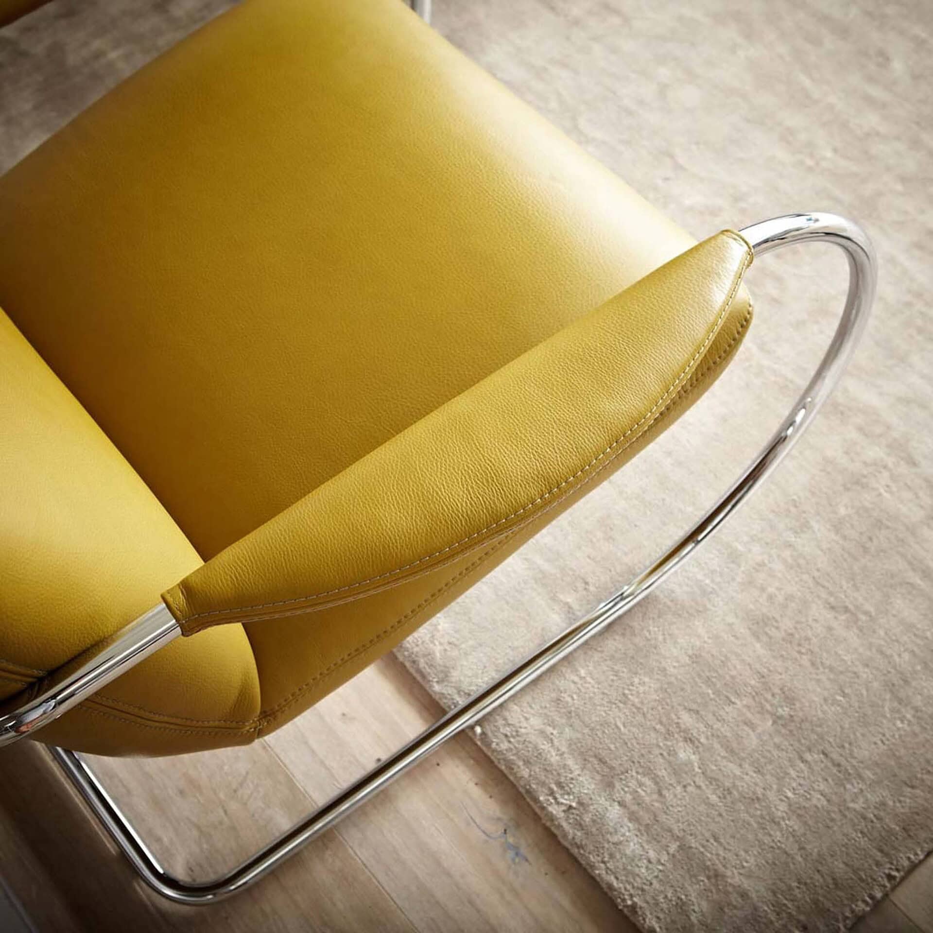 Detail close-up of the Jumper Cantilever Armchair in yellow fabric and chrome frame.