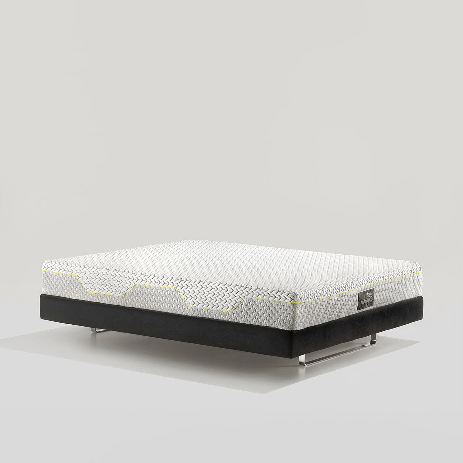 A white and grey textured mattress with yellow accents on a black upholstered bed base with polished chrome legs, set against a light grey background.