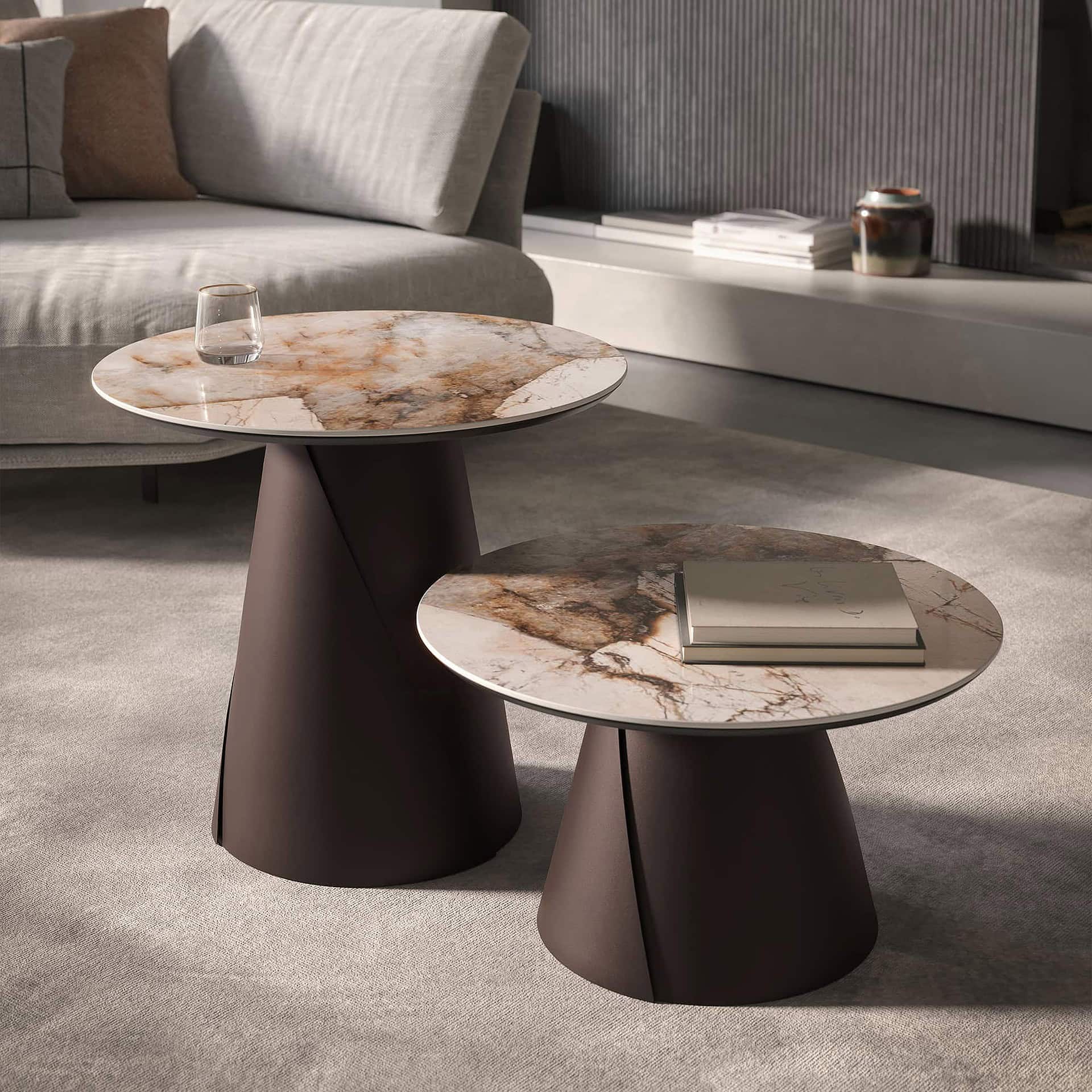 Two modern round side tables with veined marble tops and dark brown tapered bases, placed on a light grey rug in a contemporary living room with a grey sofa and minimalist decor.