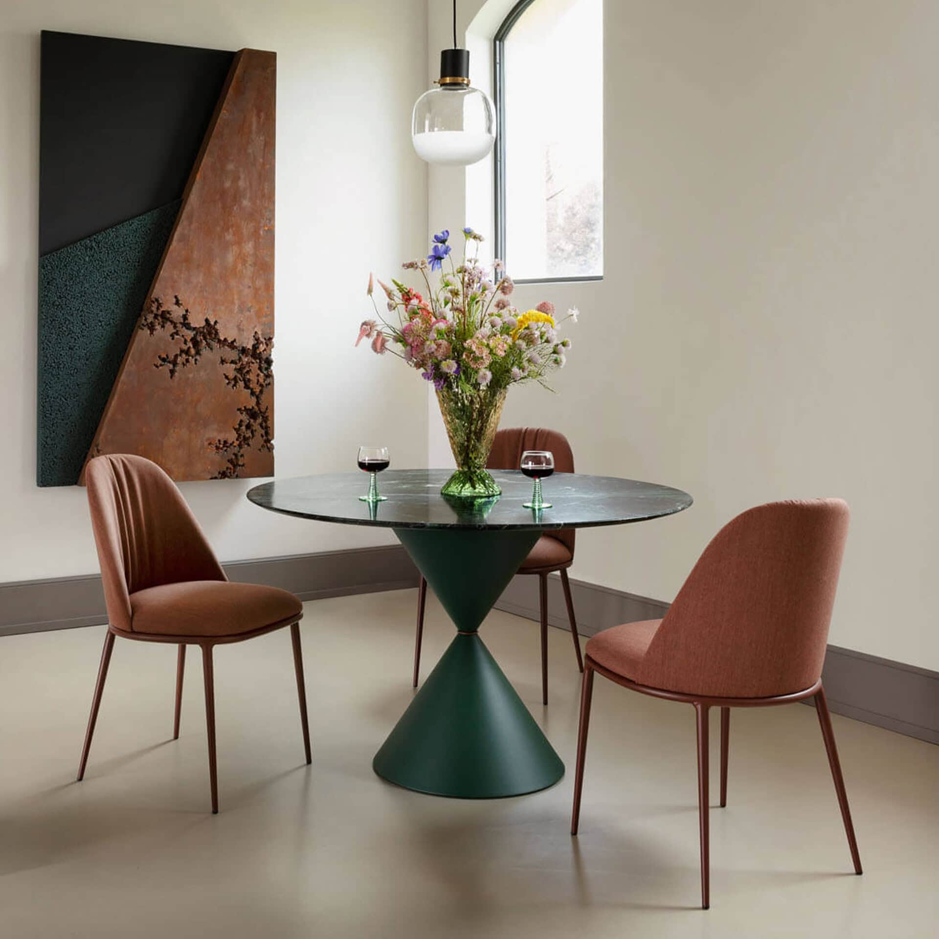 Modern round dining table with pink upholstered chairs and a floral centerpiece in a bright, minimal.