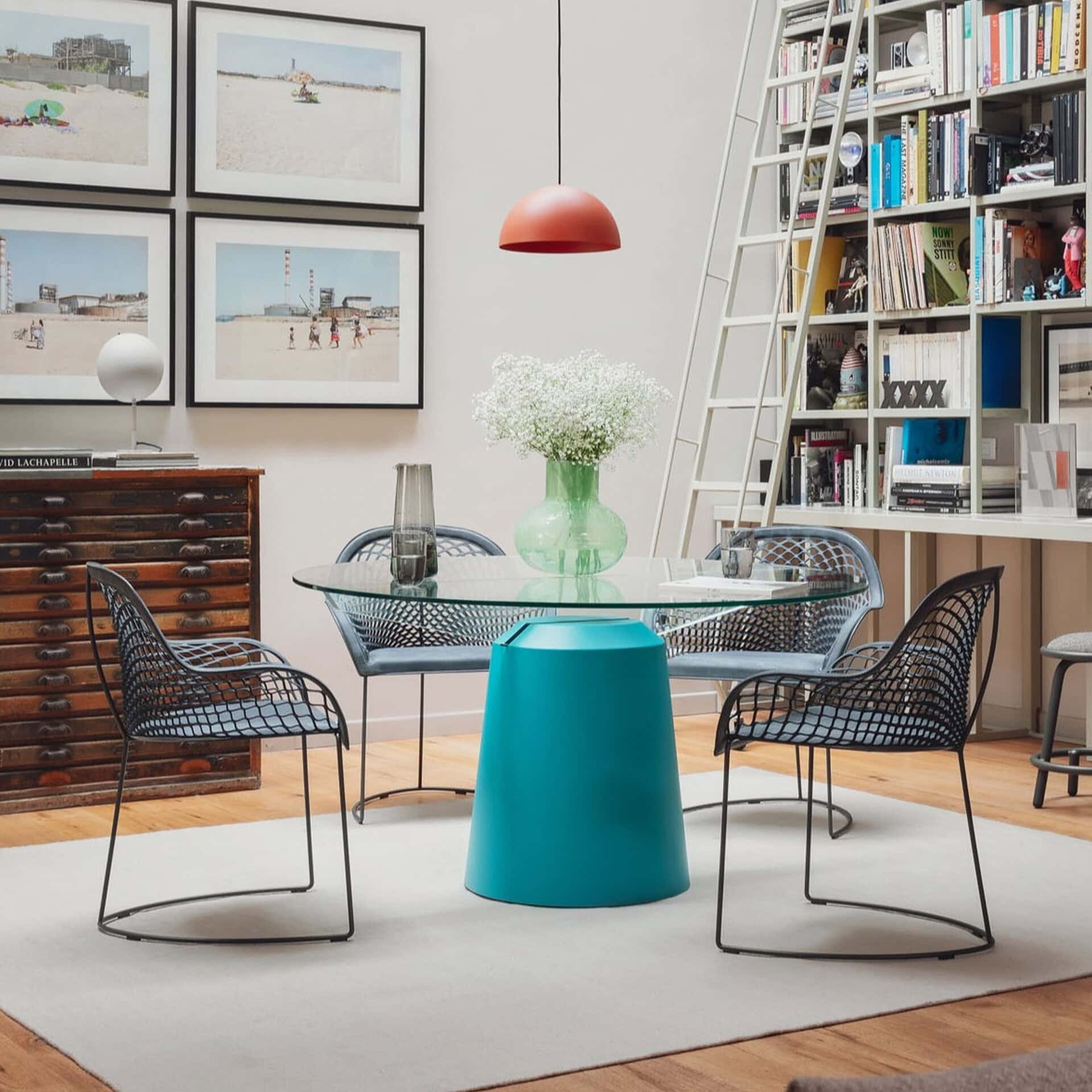 Contemporary glass dining table with black wire chairs in a modern living room.