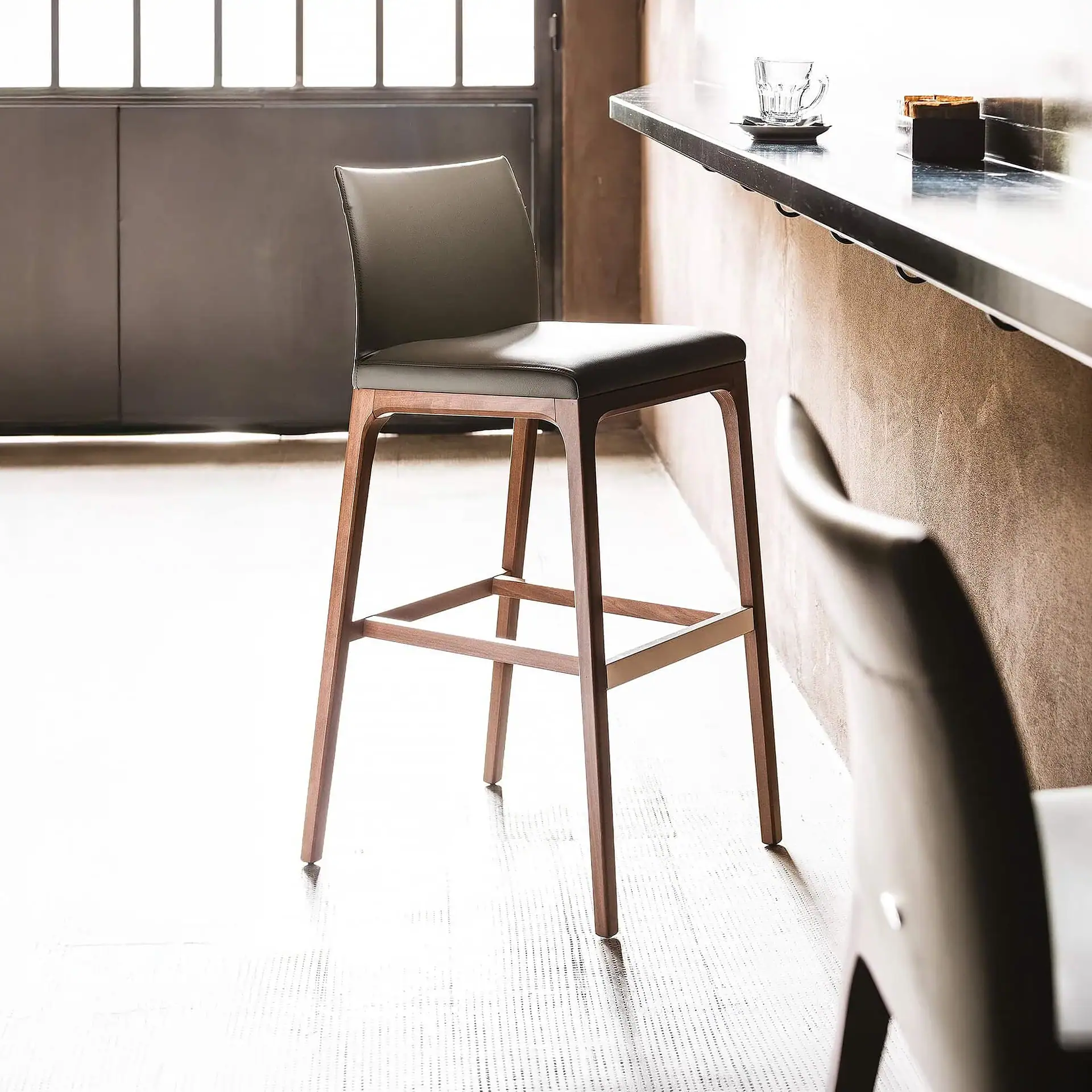 Sklar Furnishings Arcadia bar stool with black upholstery and wooden legs.