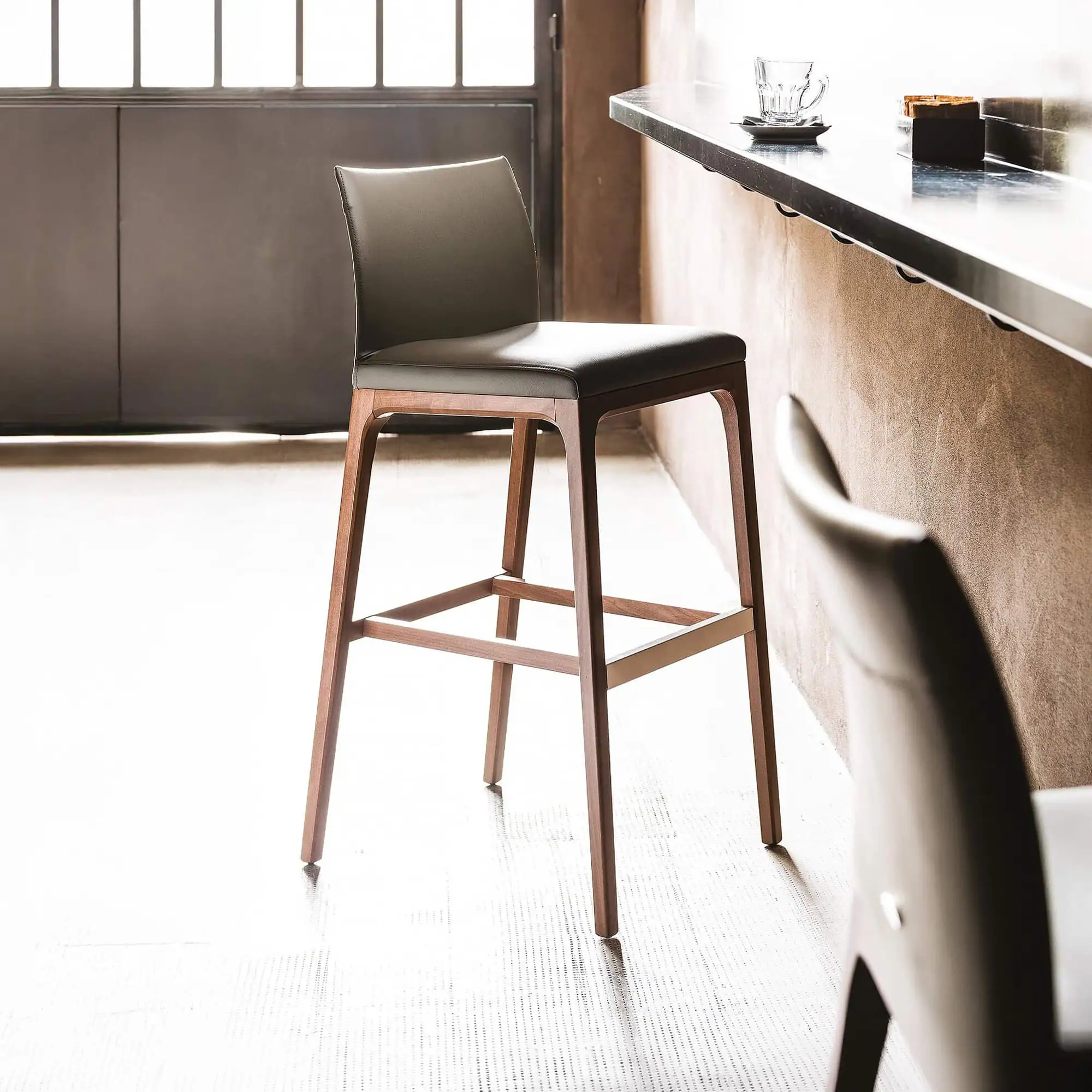 Sklar Furnishings Arcadia bar stool with black upholstery and wooden legs.