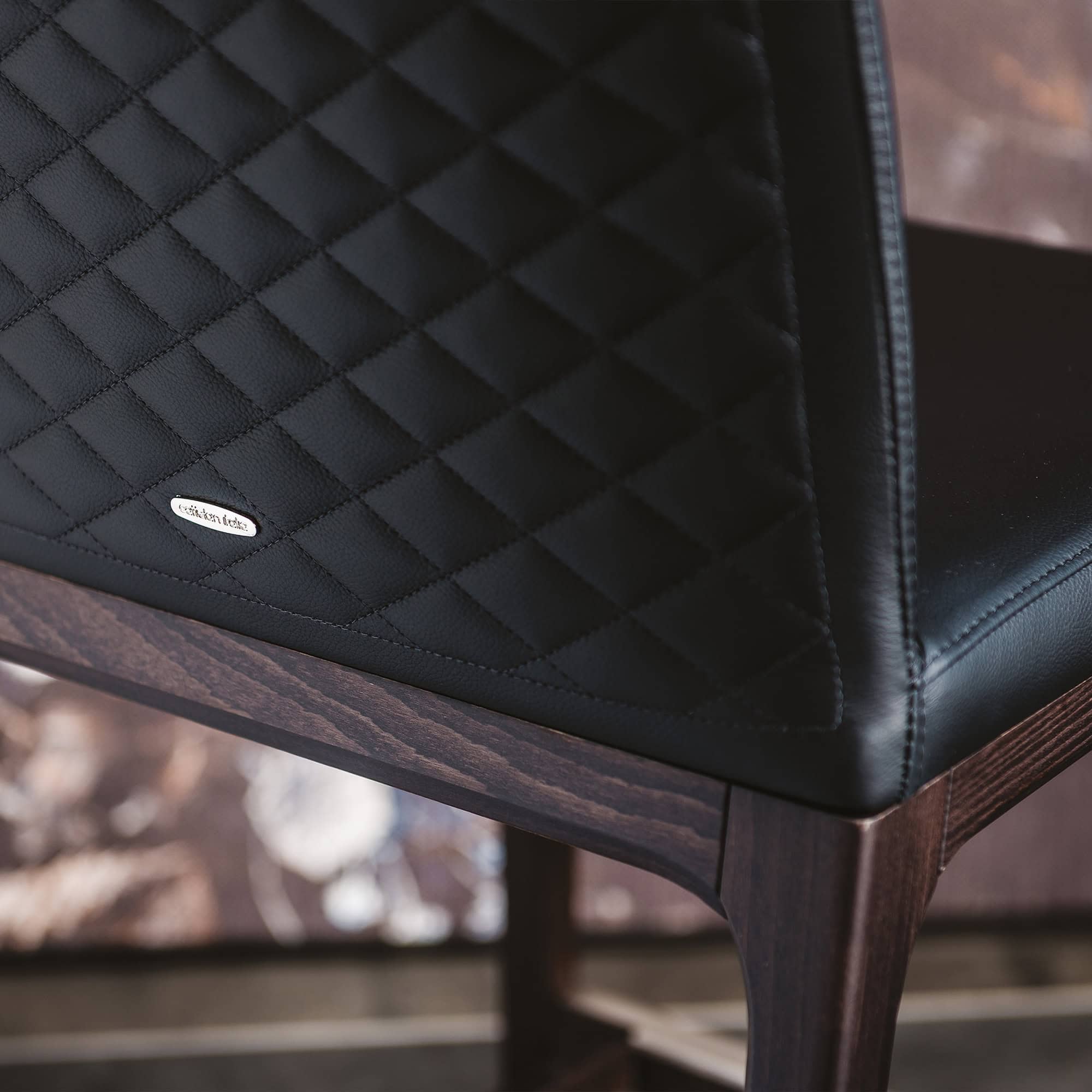 Luxurious black quilted leather upholstery on a wooden dining chair by Sklar Furnishings.
