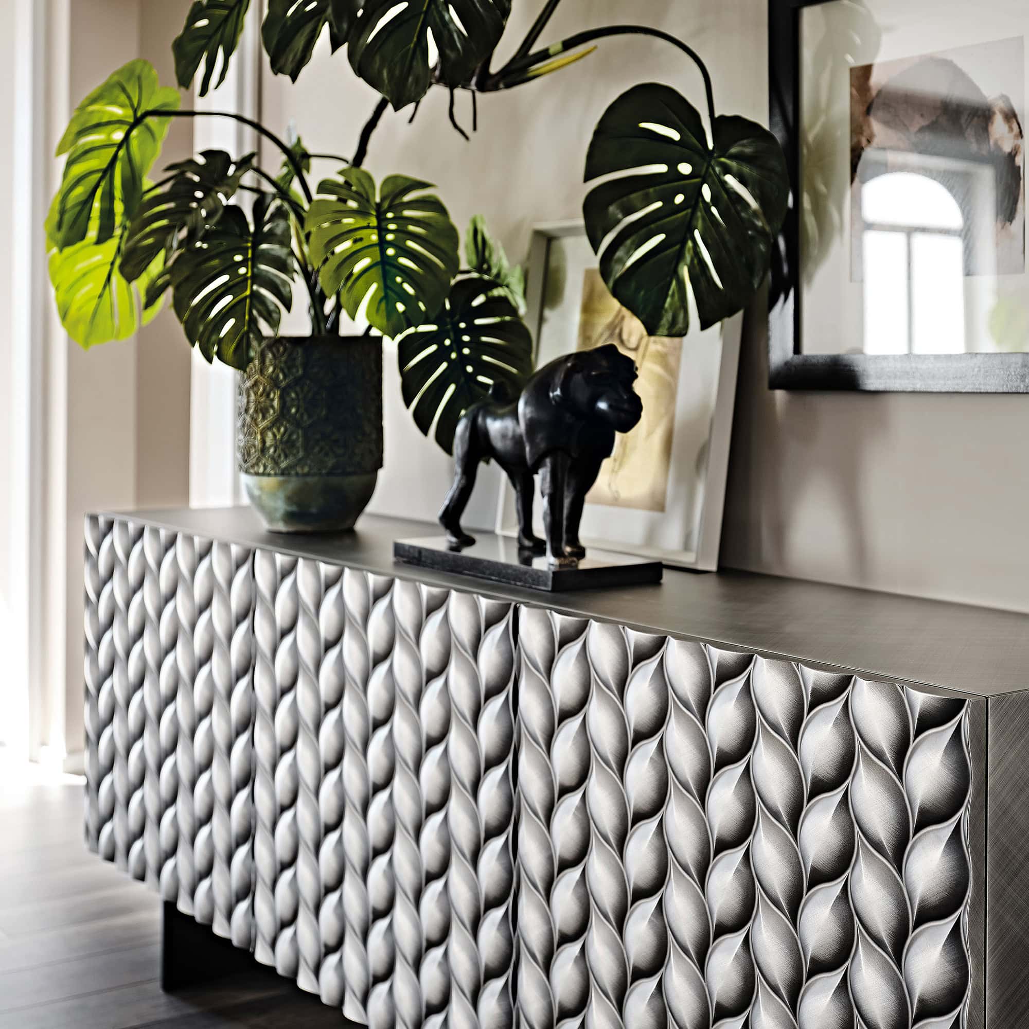 Elegant sideboard with textured leaf pattern and decorative accents, including a potted plant and artwork, from Sklar Furnishings.