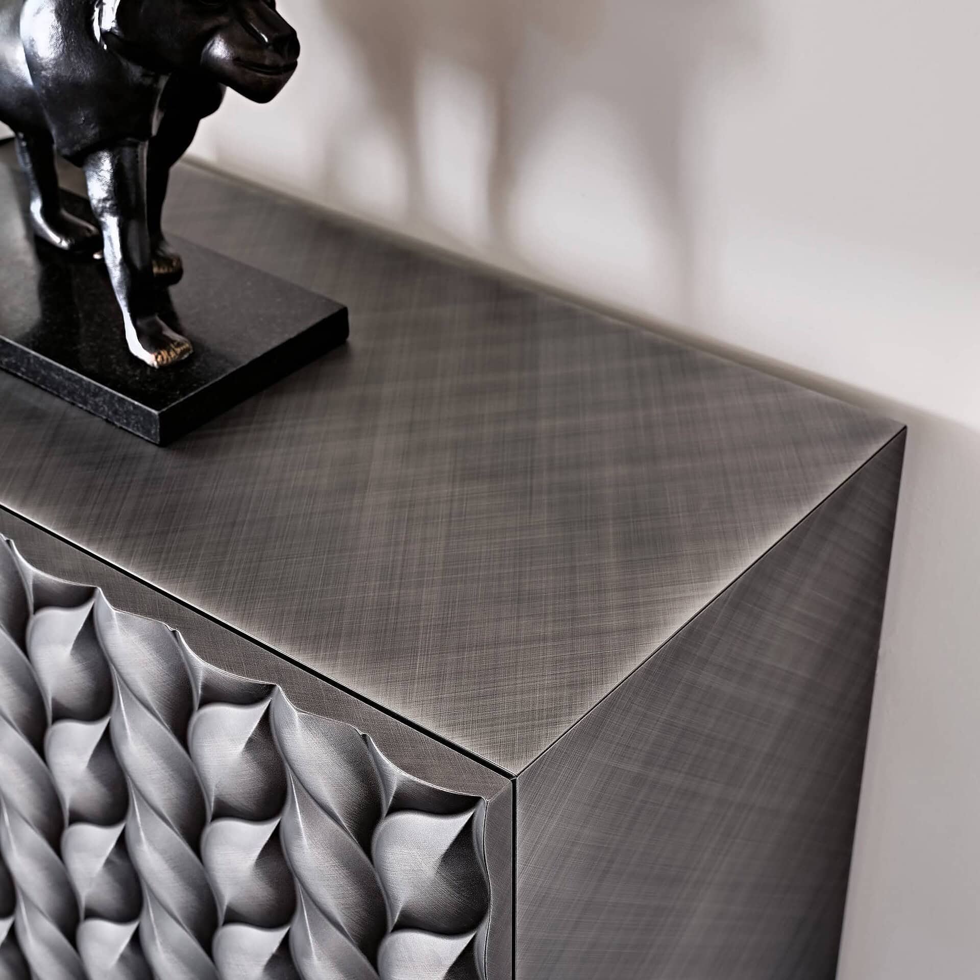 Polished stainless steel sideboard with textured geometric front design and decorative black sculpture.