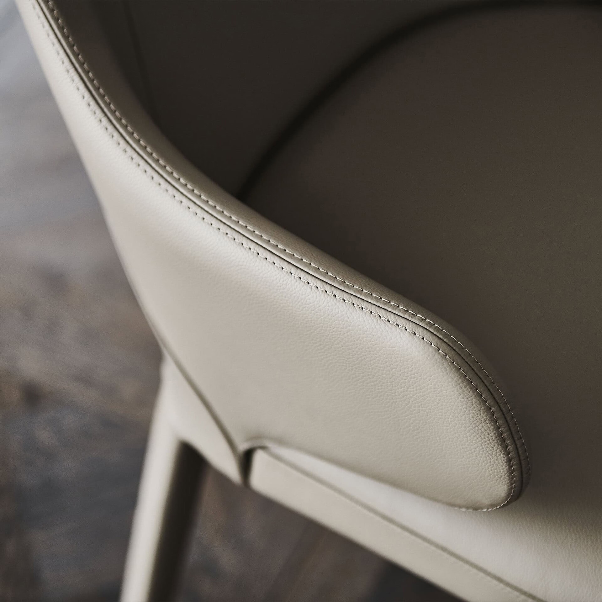 Sleek beige leather upholstered dining chair with detailed stitching and modern design.