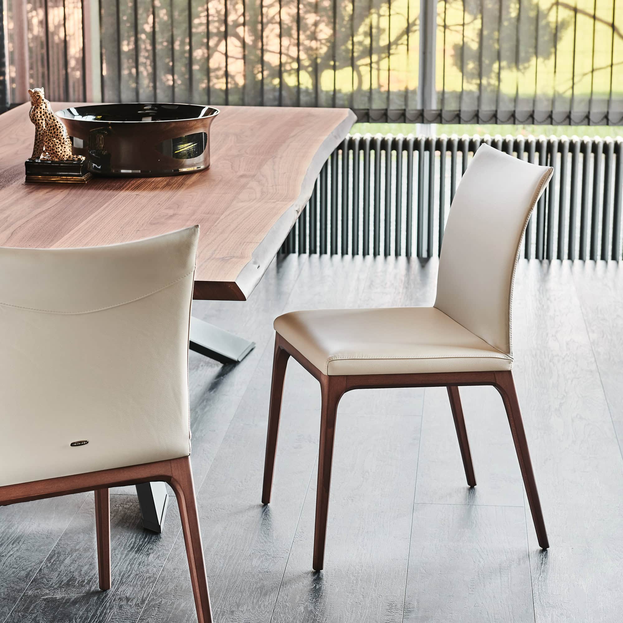 Pair of Arcadia Low Back Dining Chairs in Cenere leather with walnut legs, set around a wooden dining table
