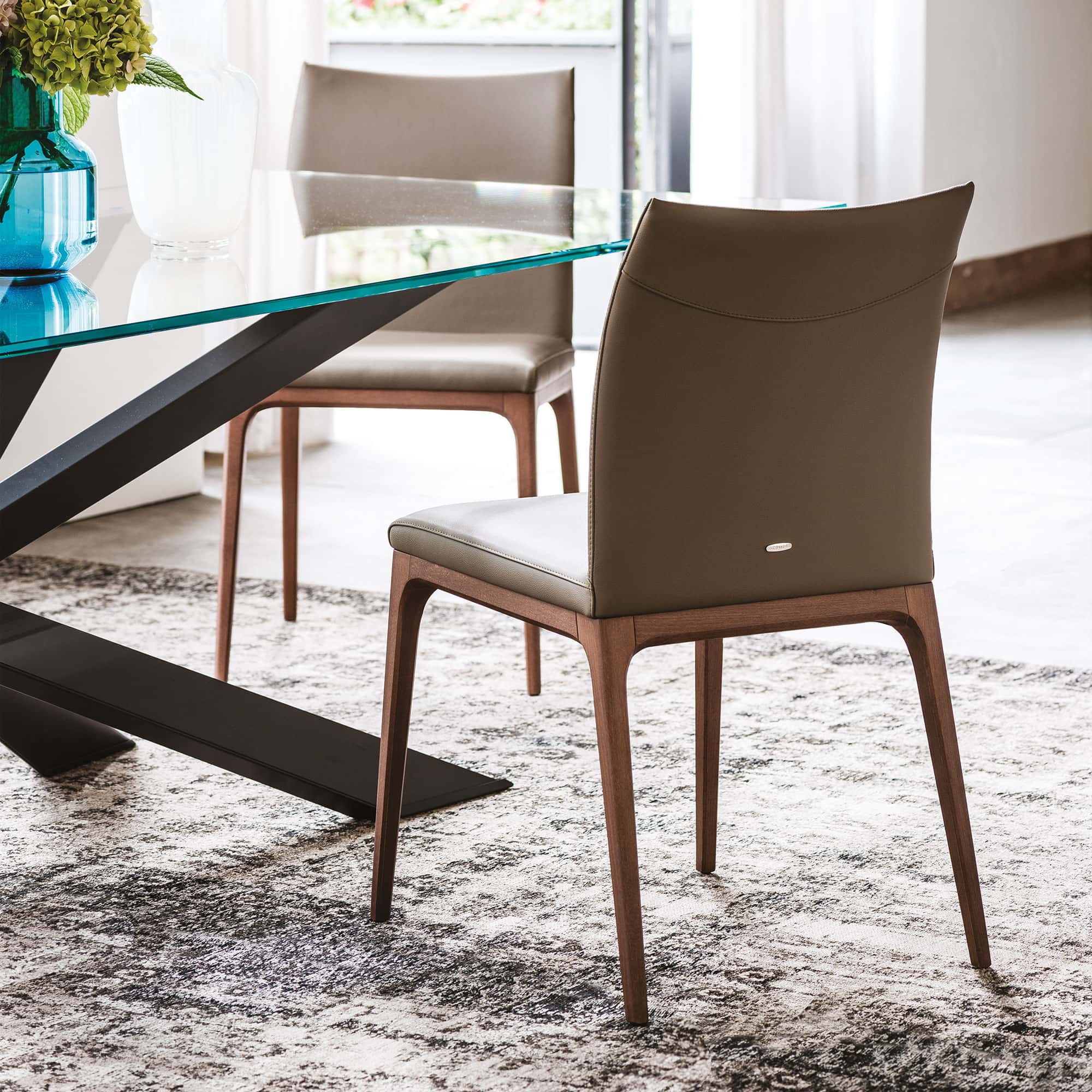 Arcadia Low Back Dining Chair in Cenere leather with walnut legs, paired with a modern glass dining table