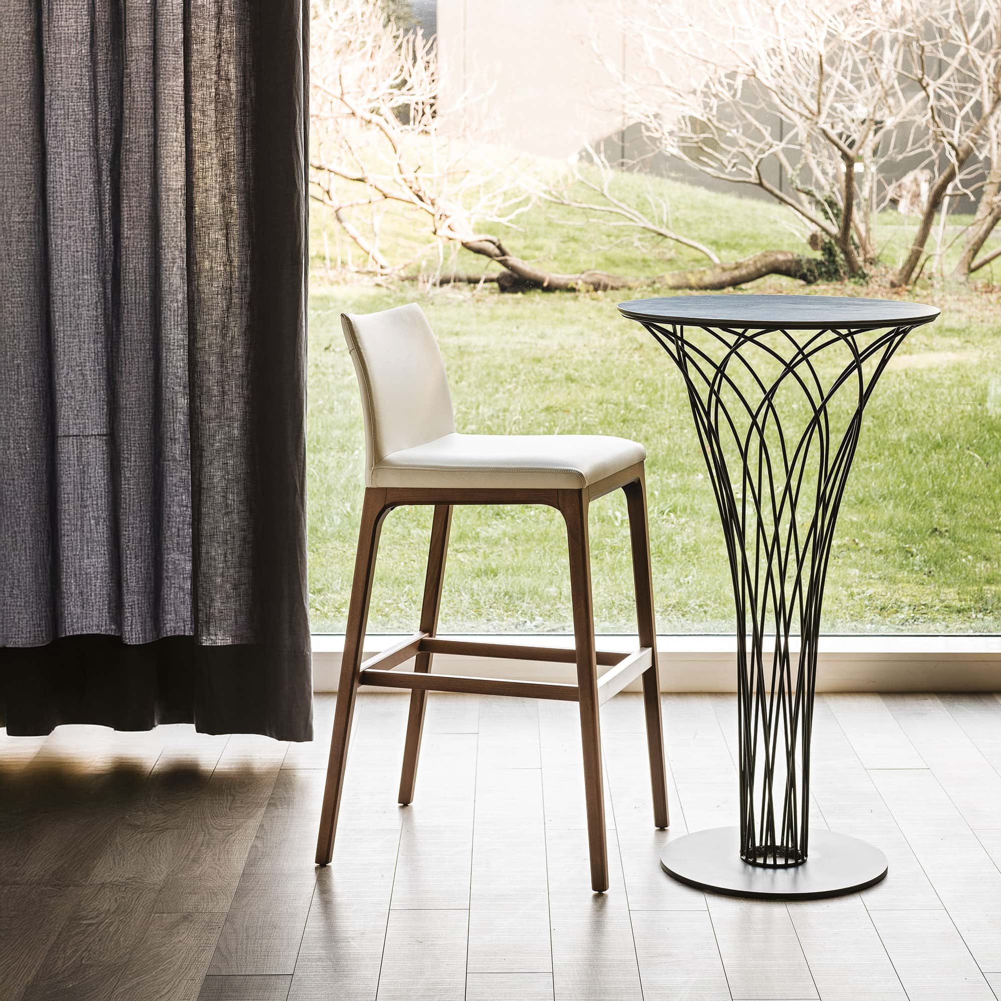 Arcadia Stool beside a round pedestal dining table in a bright room.
