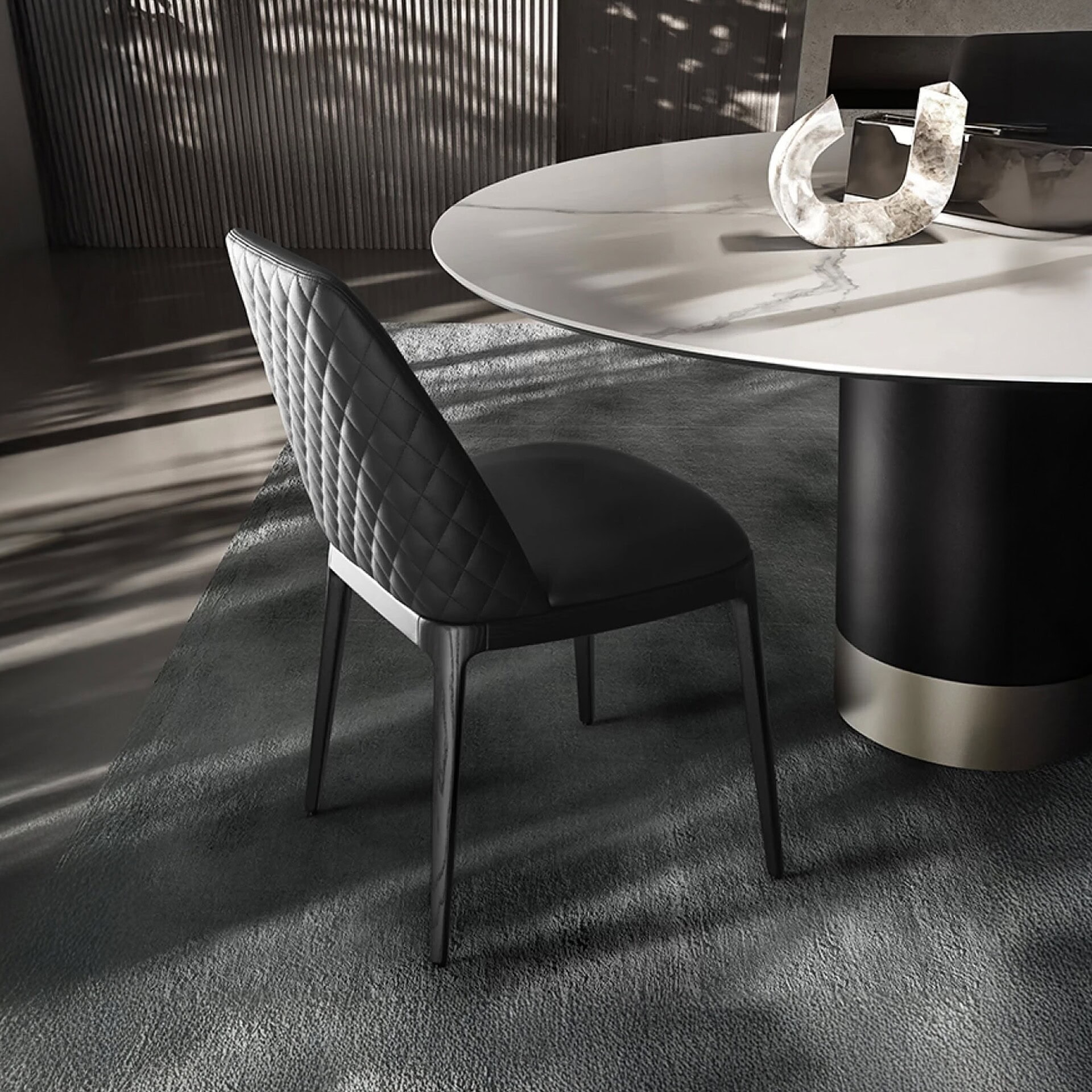 Contemporary black quilted dining chair paired with sleek marble-top table in modern interior setting.