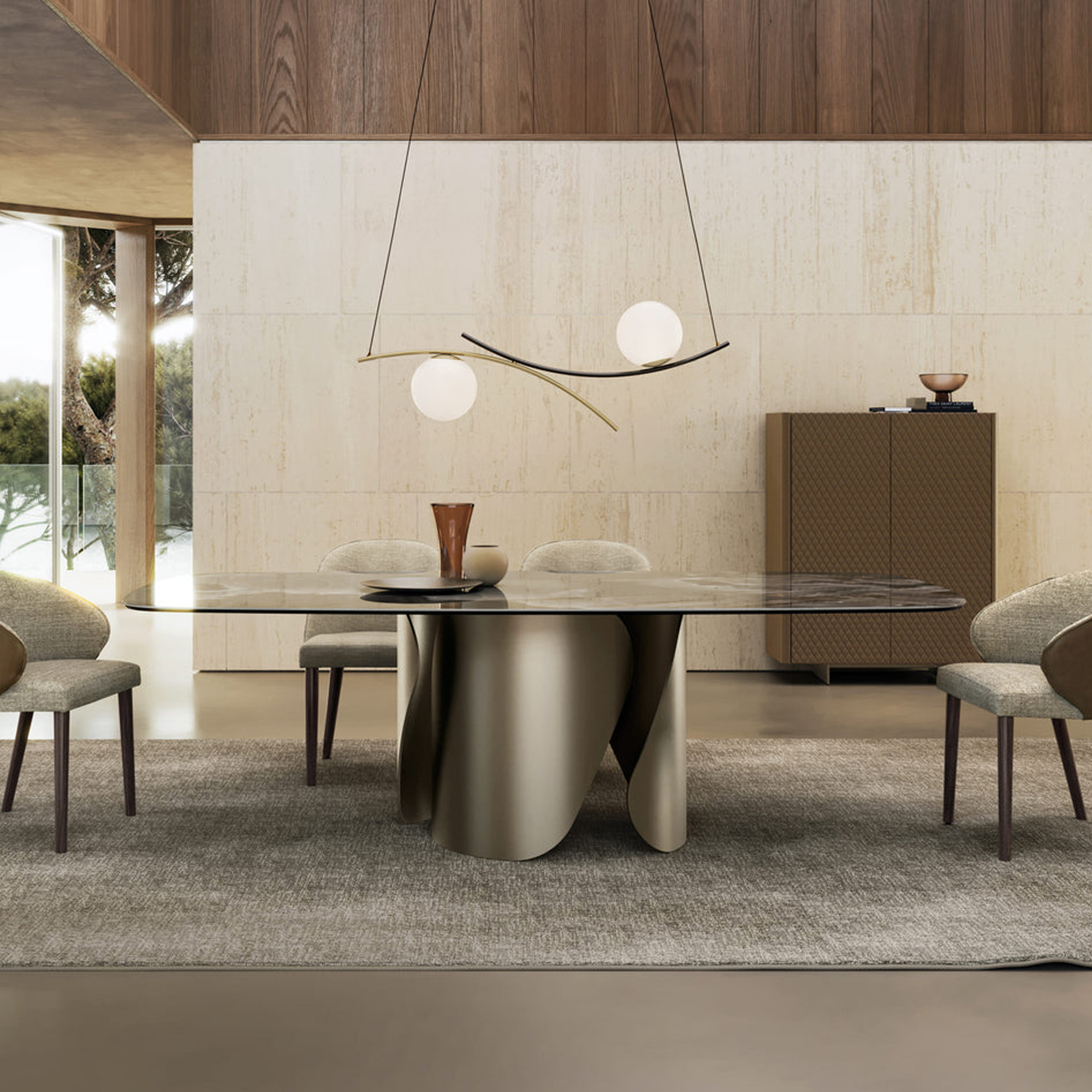 A modern dining room with a rectangular marble-top table on a sculptural metallic base, surrounded by four upholstered chairs. An abstract pendant light with two spherical globes hangs above. The room features light stone walls, dark wood paneling, a textured rug, and a dark brown textured cabinet.