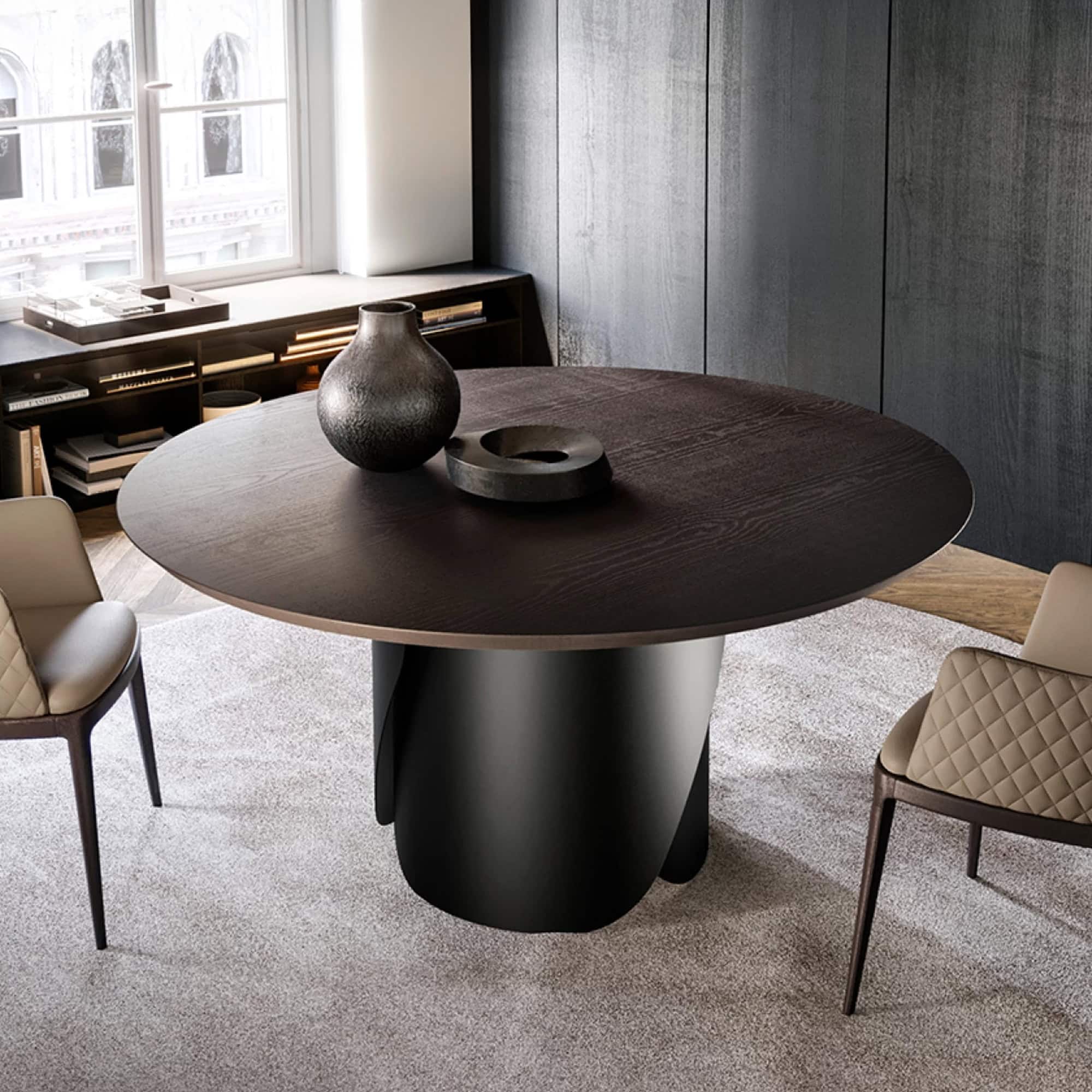 Contemporary round dining table with a dark wood top and sleek black pedestal base in a modern interior setting.