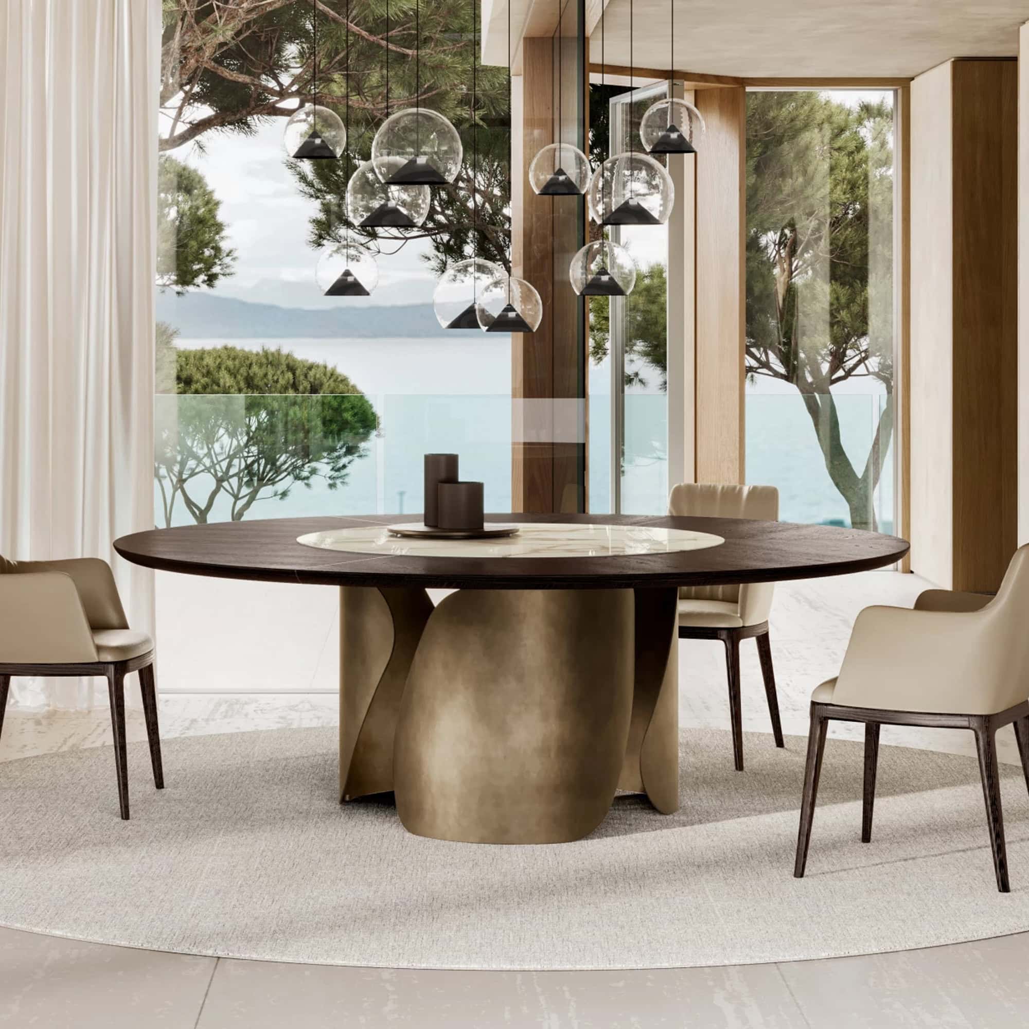 Contemporary dining room featuring a round wooden table with a modern mixed-material base and stylish chairs, overlooking scenic ocean views.