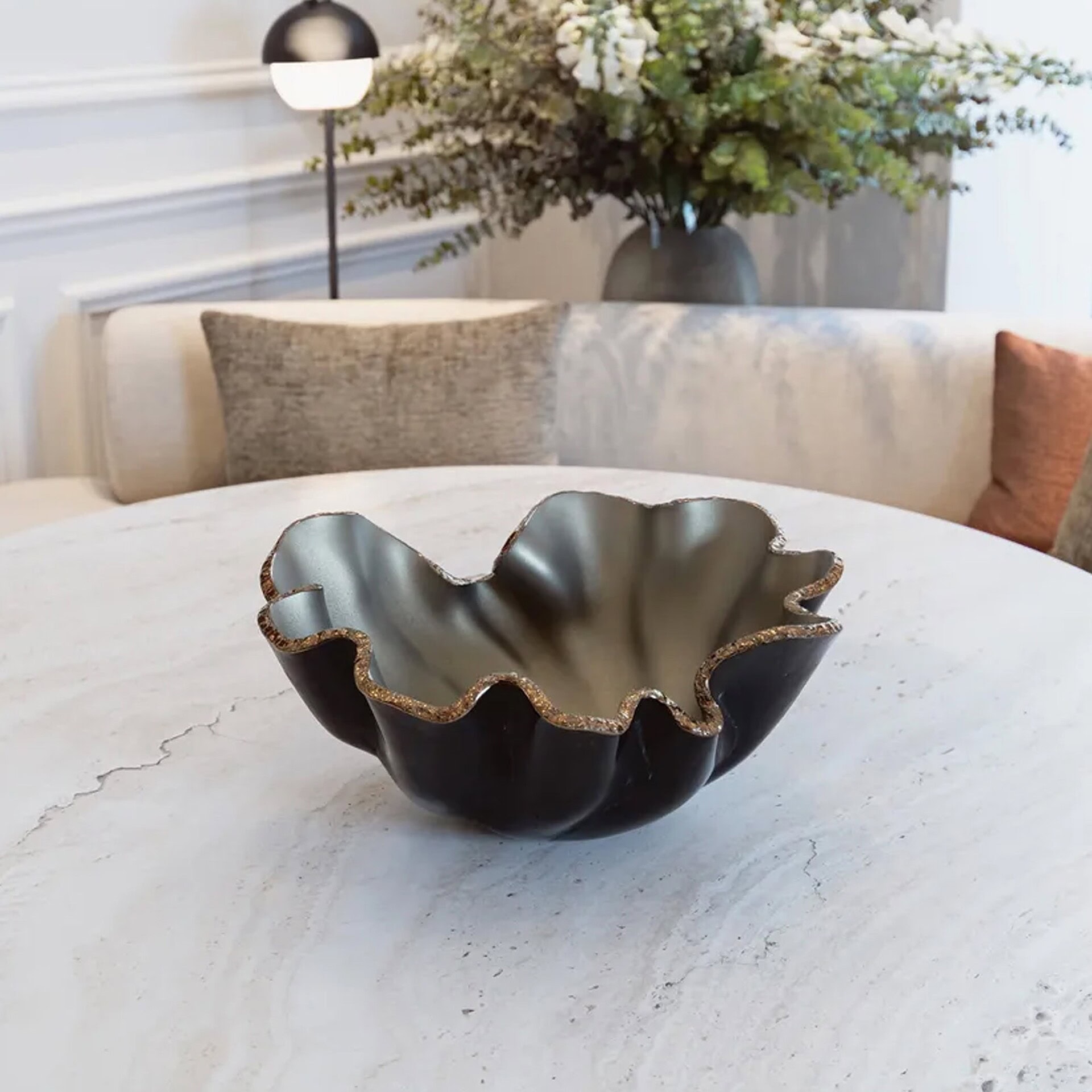 Bowl Lirio Glass Centerpiece in Perola Topo Bronze finish placed on a light stone table with floral arrangement.
