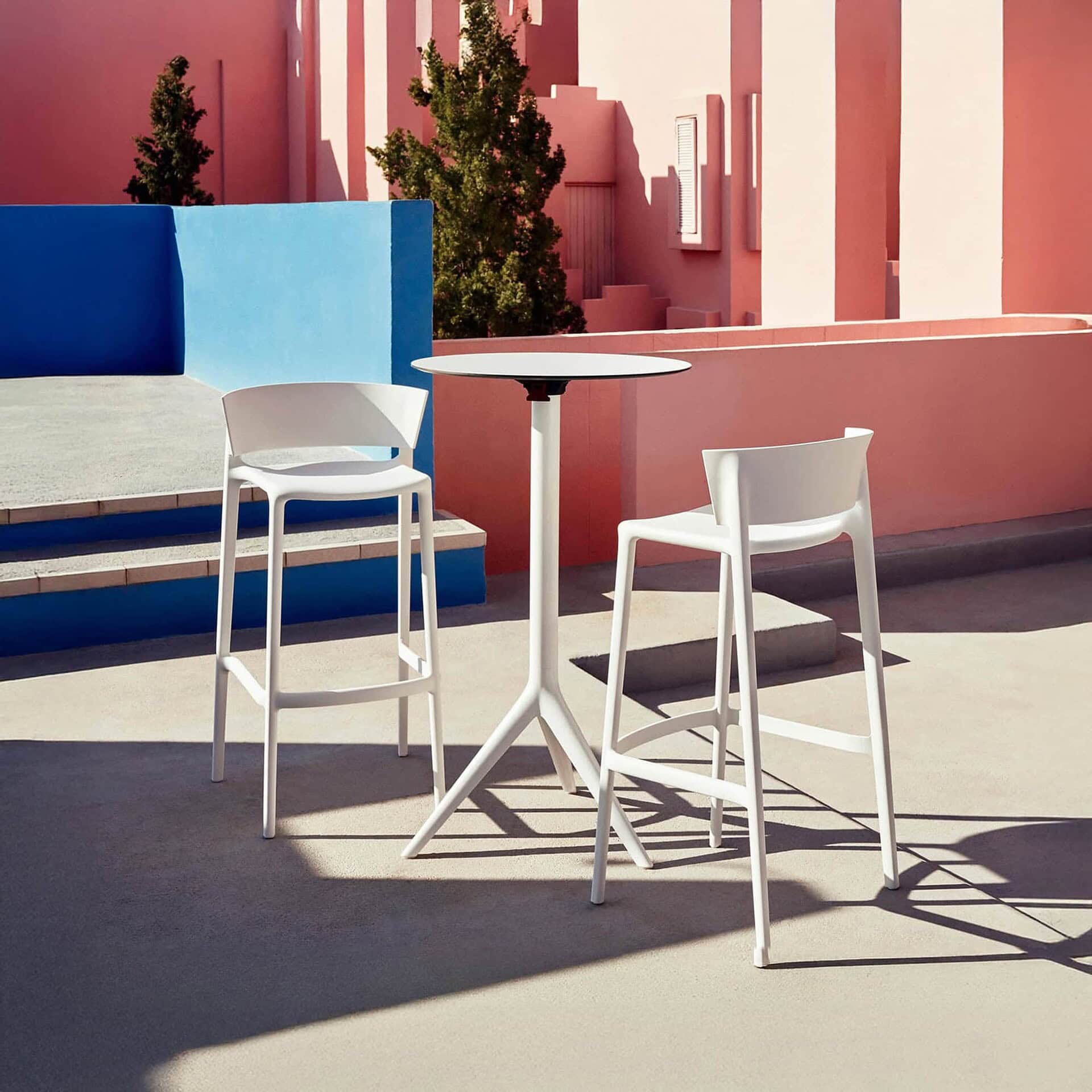 Africa Bar Stools and tables in white set against a modern pink architectural background.