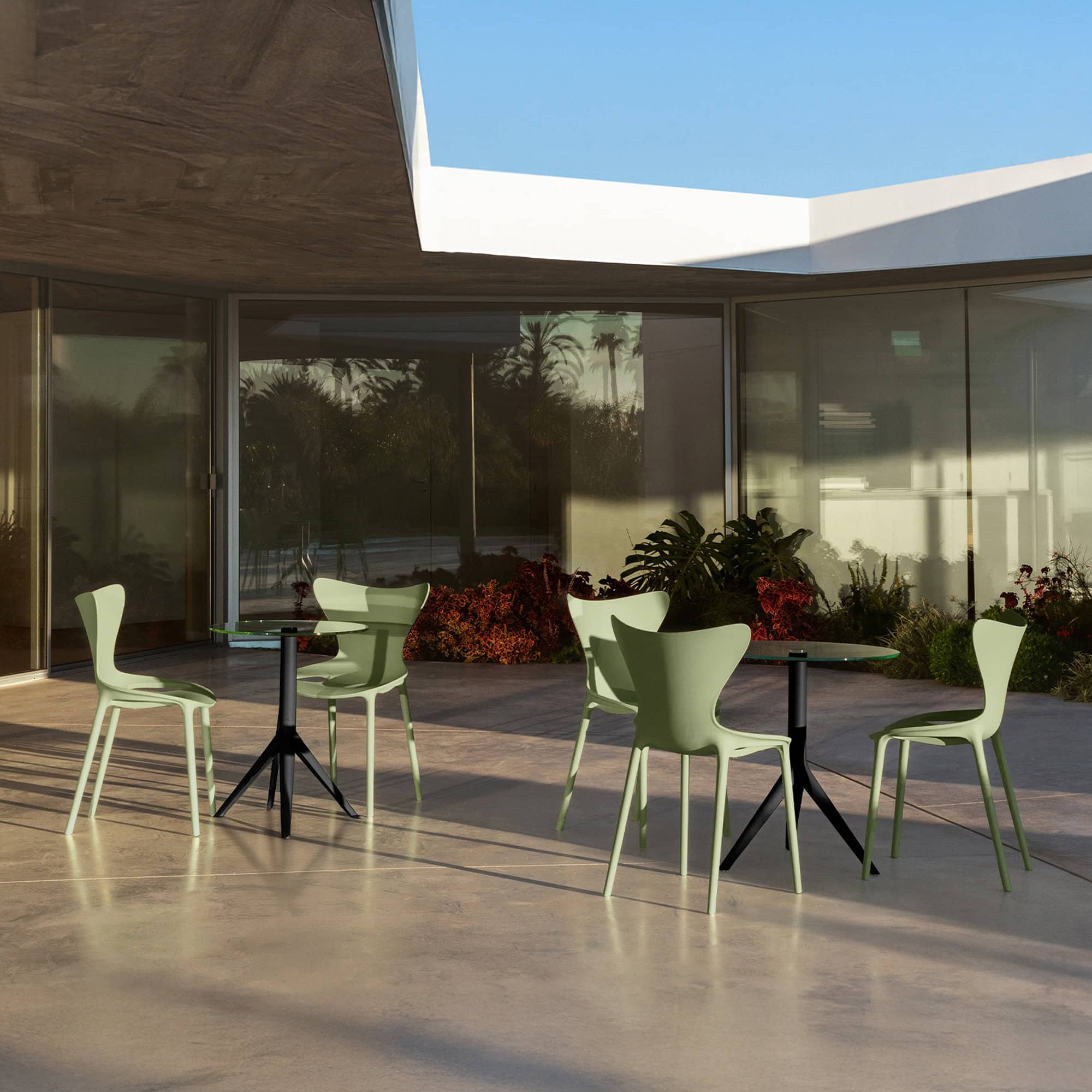 Modern outdoor patio seating with glass-topped tables and green chairs at Sklar Furnishings.