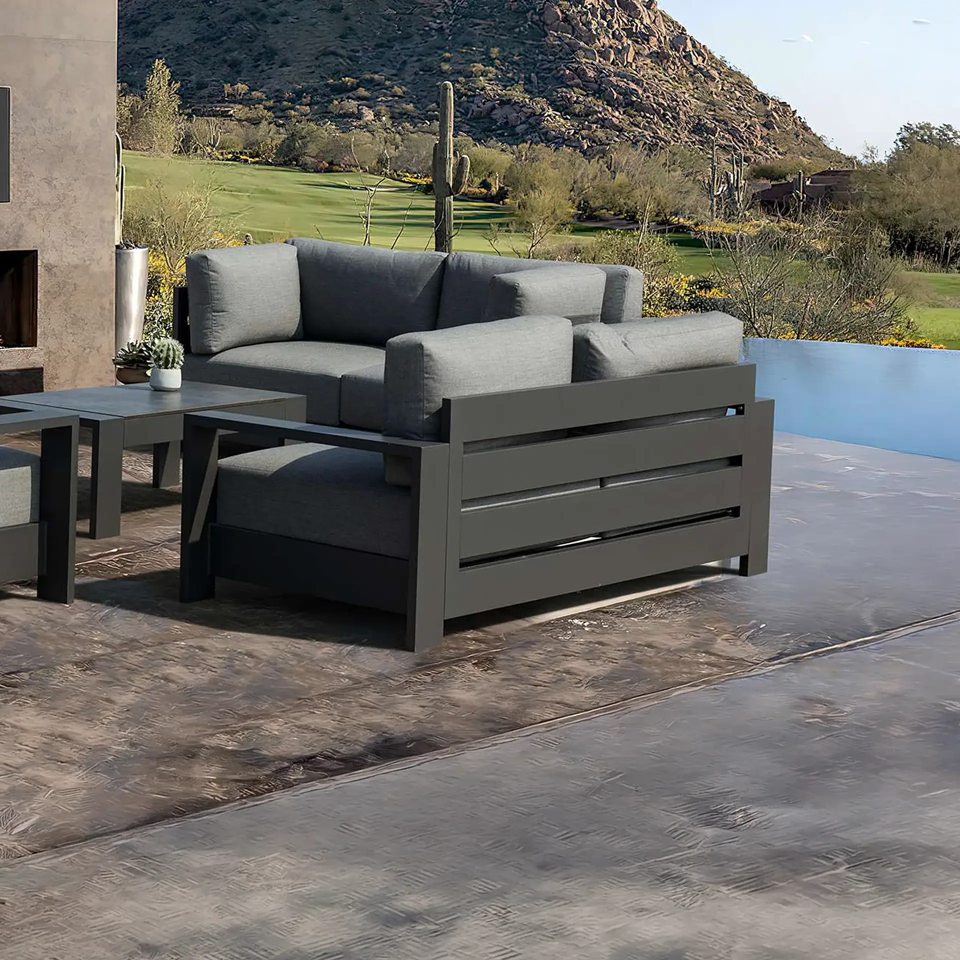 Outdoor patio with dark gray modern furniture and light gray cushions, overlooking a desert golf course, rocky mountains, and a pool.