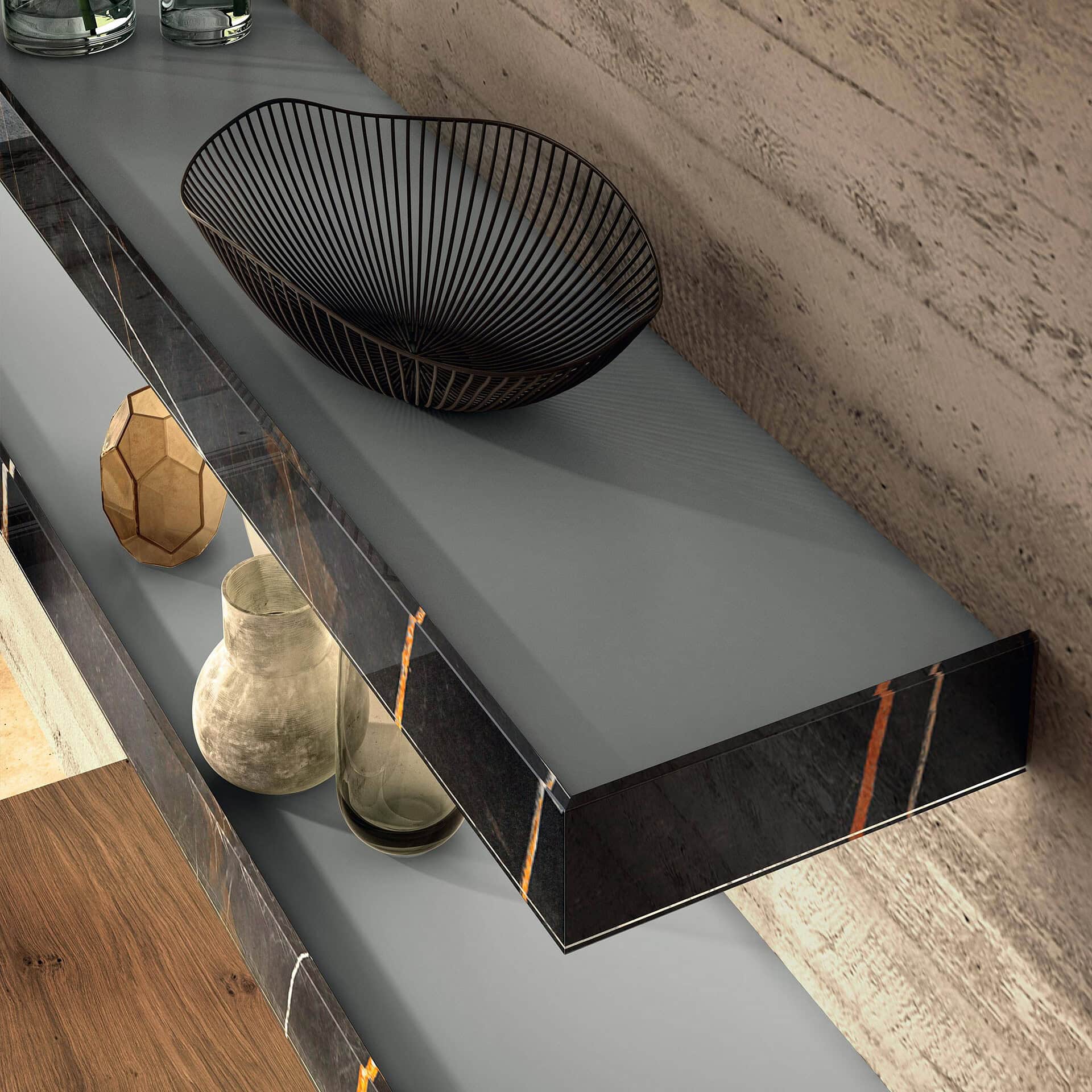Close-up of a modern grey shelf with a dark marble-effect front panel featuring orange and white veins, holding a black wire bowl. Behind it is a textured concrete wall, and below are more shelves with decorative items and a wooden panel.