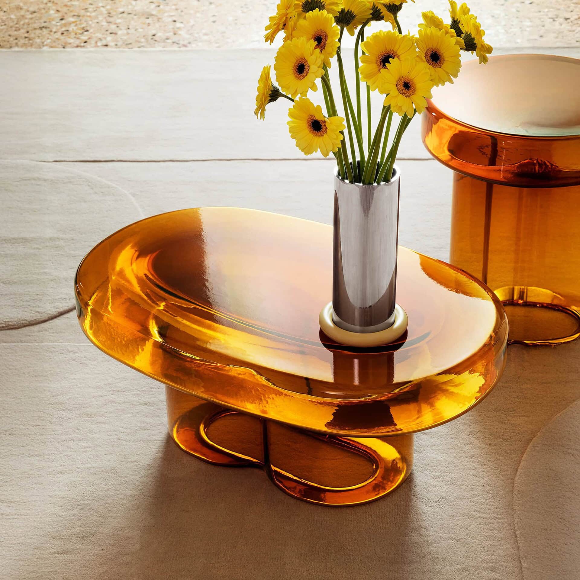 Close-up of the Soda Oval Coffee Table in Amber glass with a vase of yellow flowers.